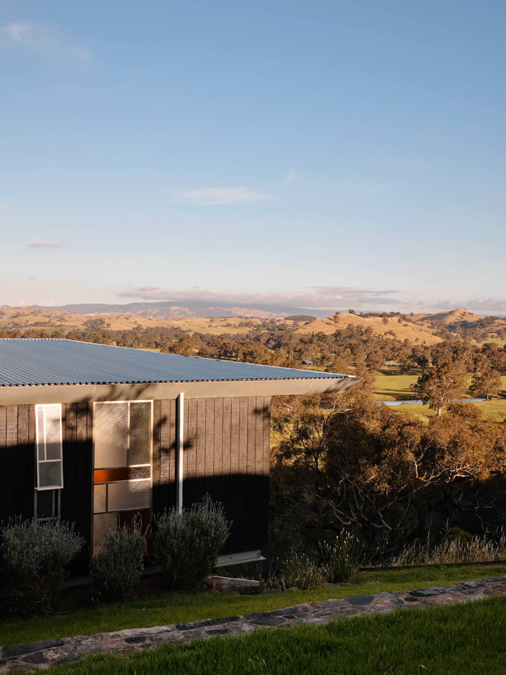 A modern house with a wooden exterior and metal roof in a rural landscape.