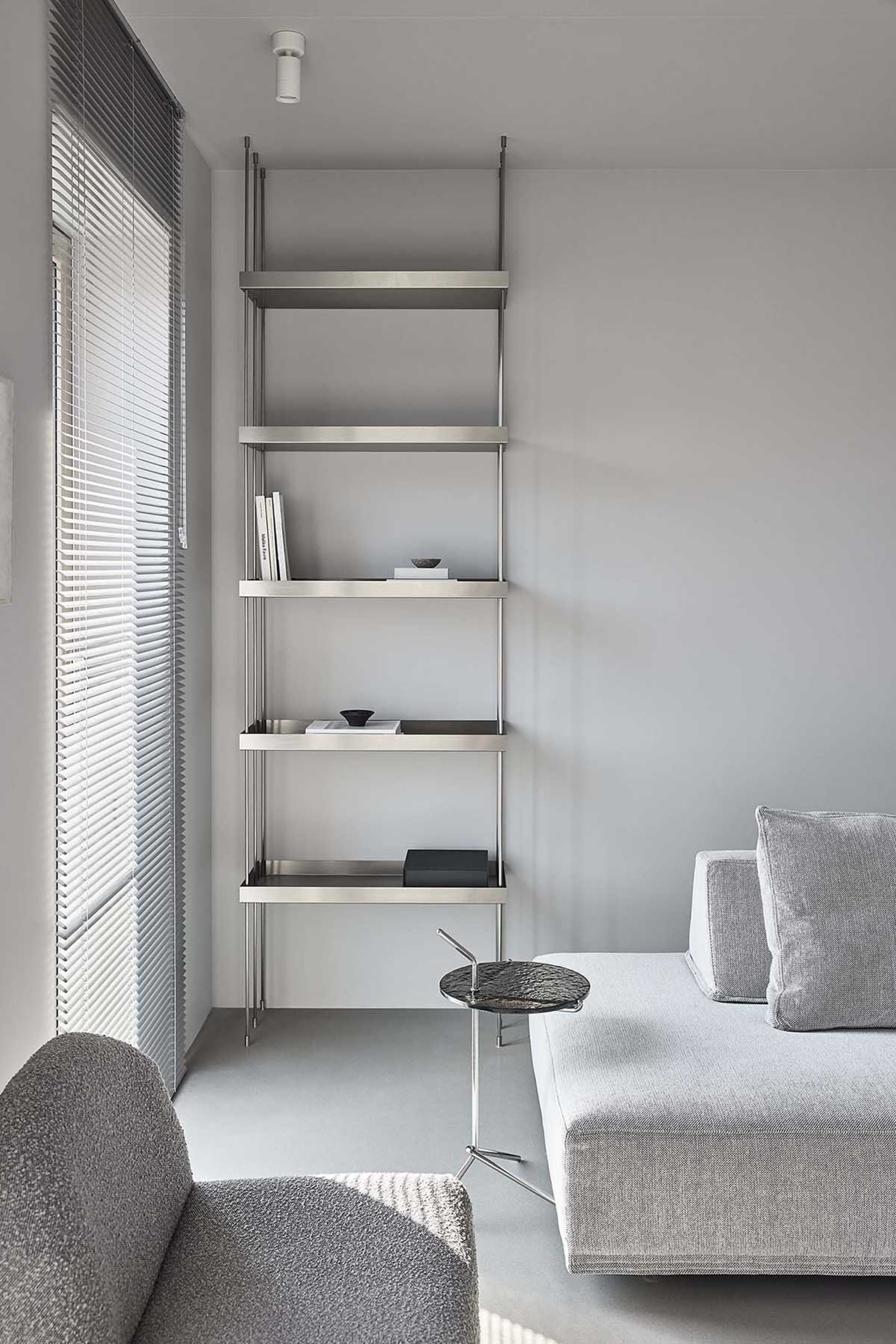 A modern interior design featuring minimalist metal shelving unit against a gray wall and a gray sofa with a side table.