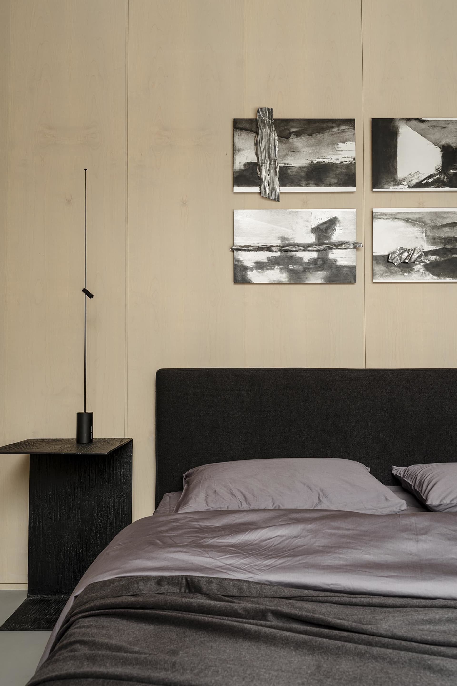 A minimalist bedroom with a bed featuring a textured fabric gradient and a black headboard, accompanied by abstract art piece
