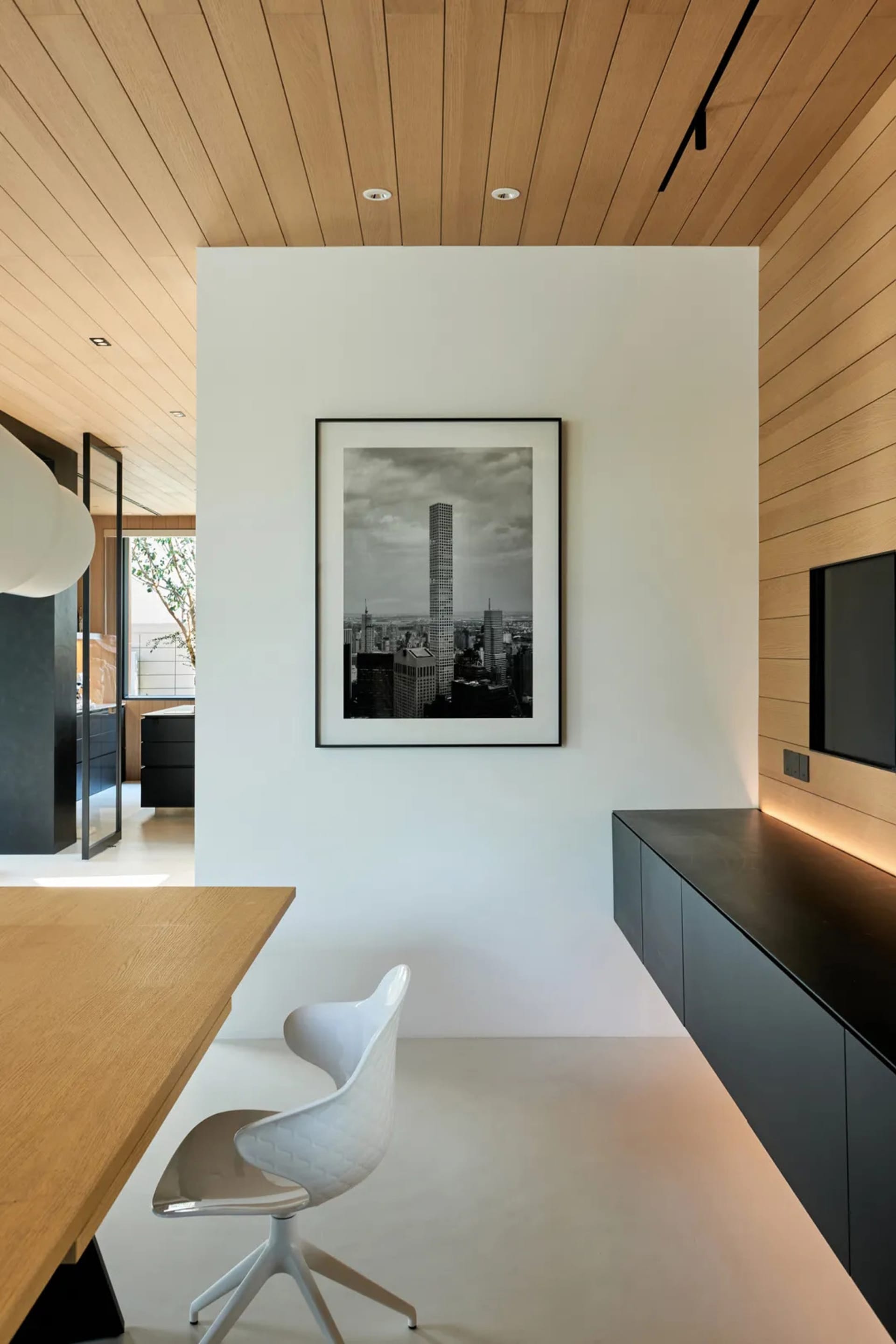 A home office with a modern design featuring a white chair and a wooden desk, with a black and white photograph of a cityscap