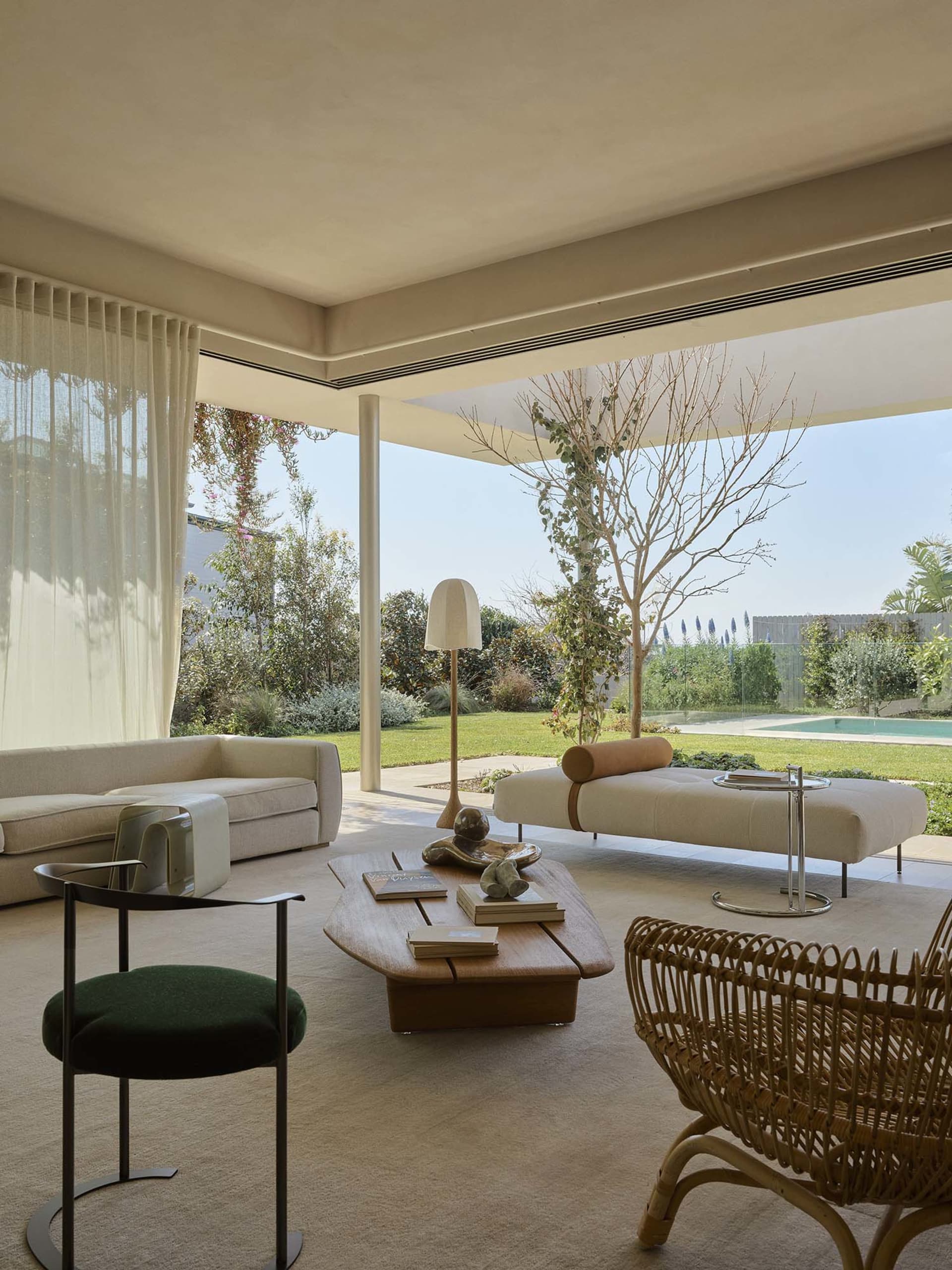 Modern living room featuring a woven armchair, fabric sofa, wooden table, and glass lamp. Bright, spacious, and contemporary.