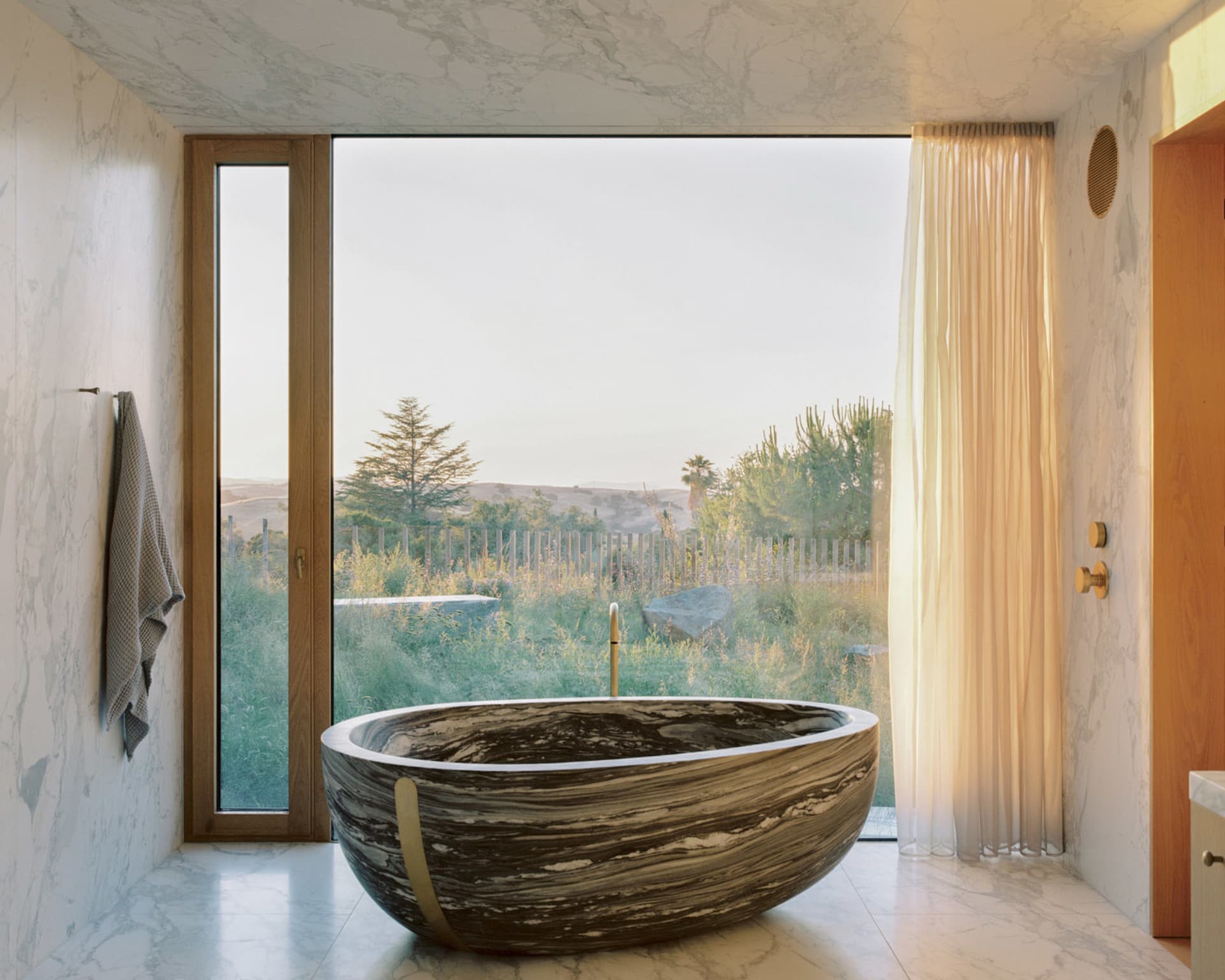 Modern residential bathroom with a large marble tub and a view of the outdoors