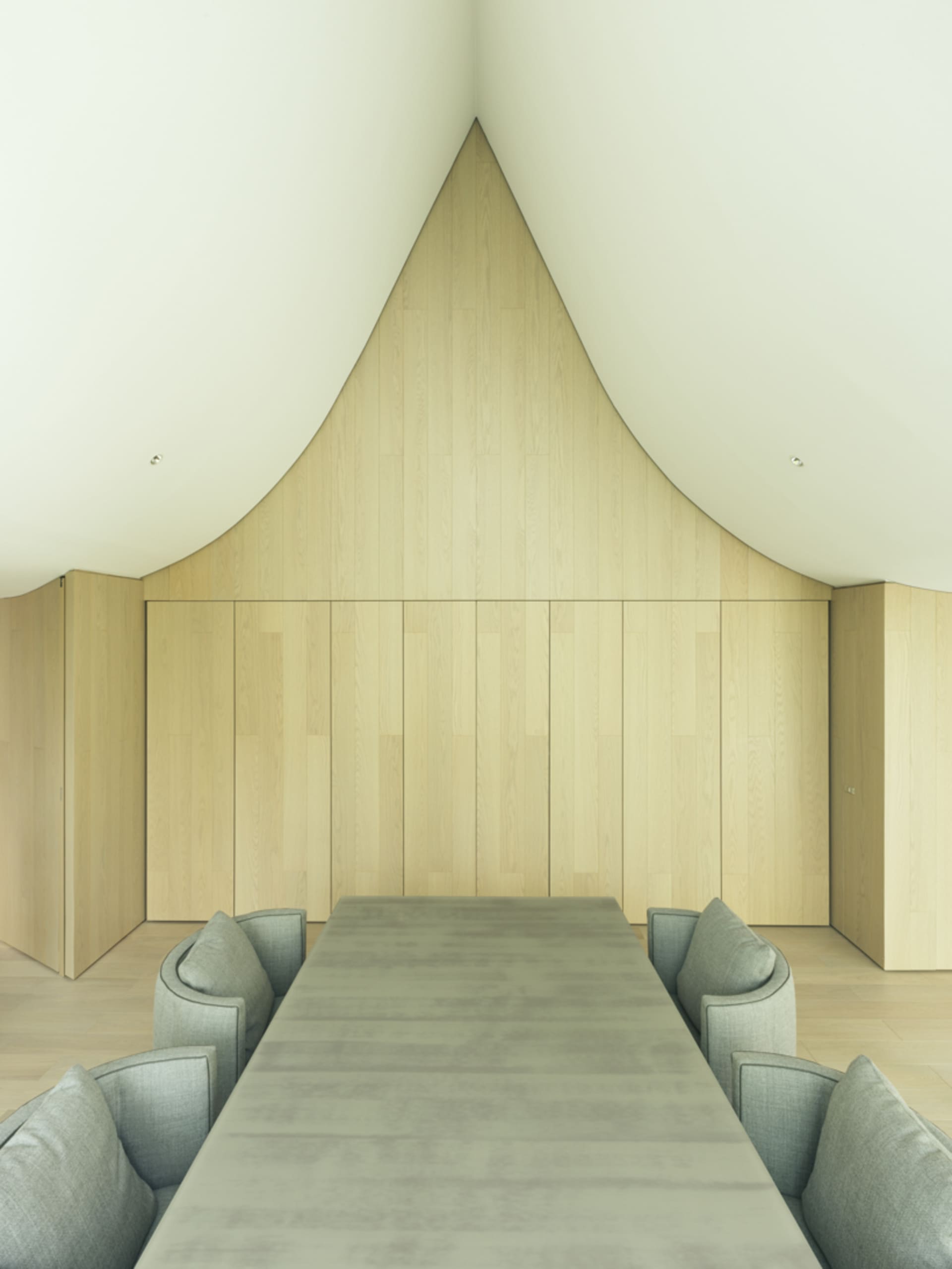 A modern interior space with minimalist design, featuring a wood paneled ceiling and a long, sleek dining table surrounded by