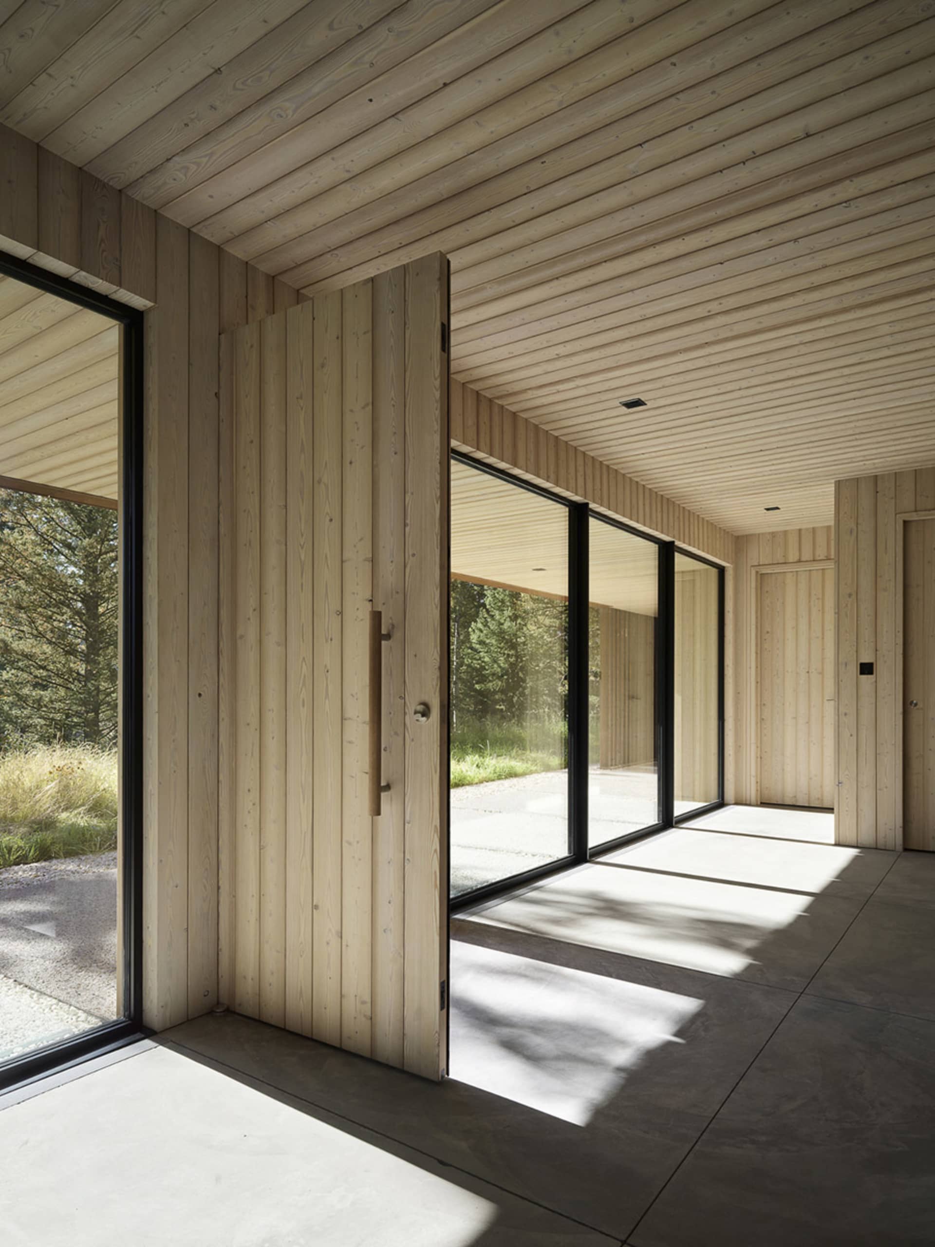 Modern interior design with wooden walls and floor, large glass windows, and concrete flooring.