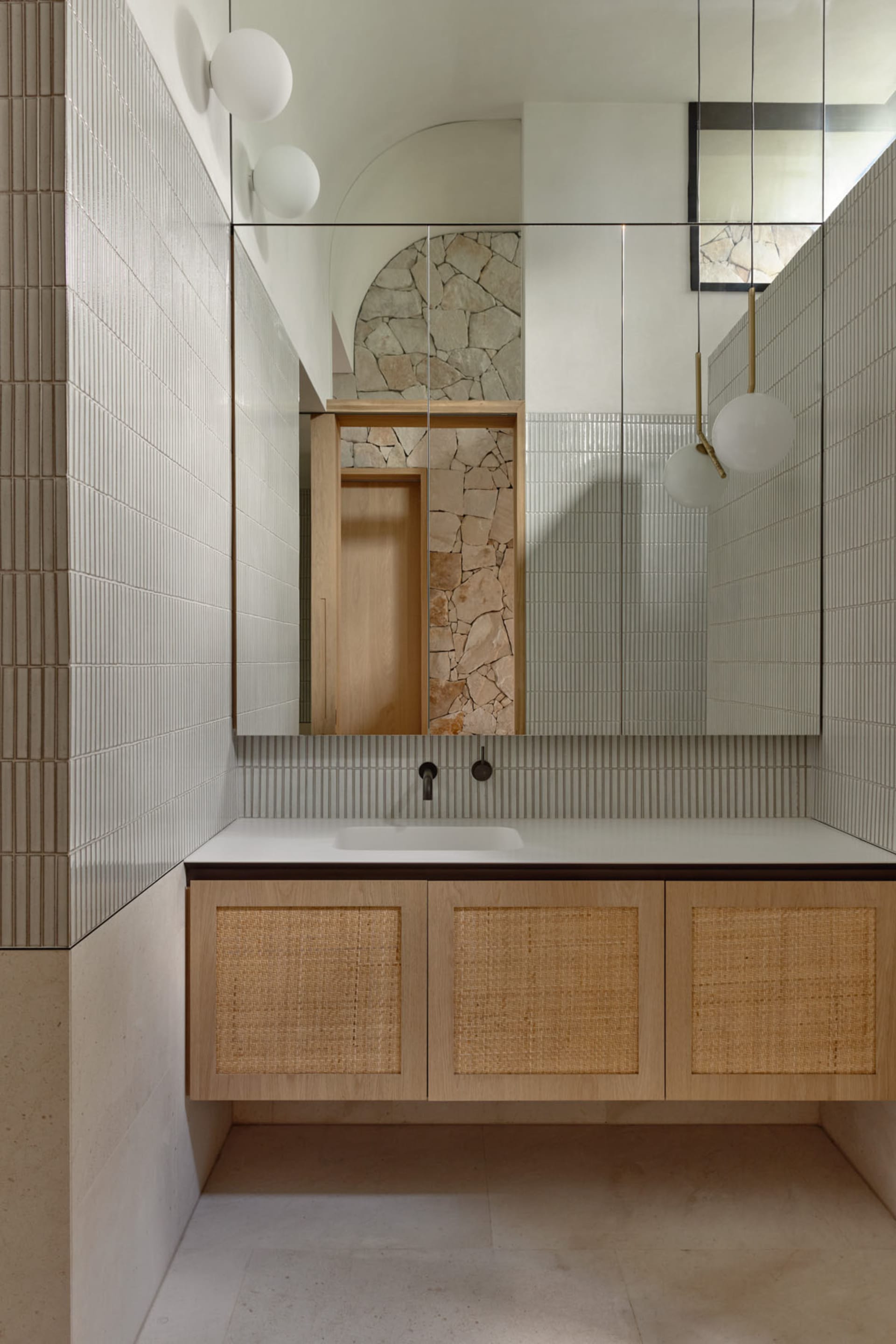 Modern bathroom interior with white textured ceramic tiles, floating wooden cabinet with woven wicker doors, and a minimalist