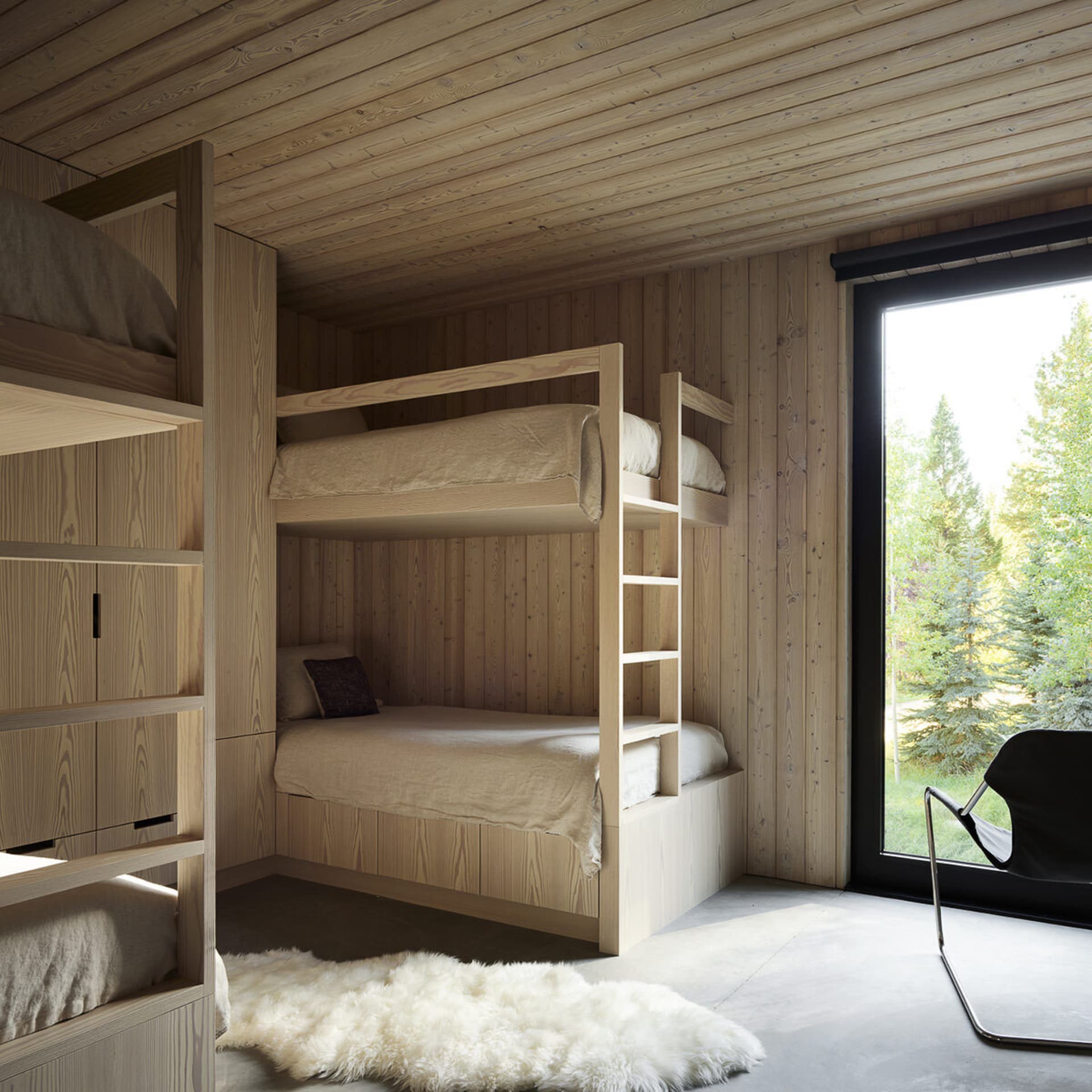 A modern bedroom with wooden walls, bunk beds, and a large window showing greenery outside.