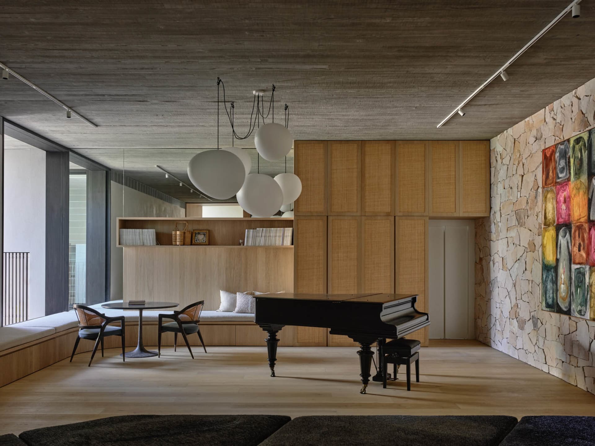 A modern living room featuring wooden furniture, a stone backdrop, and a grand piano.