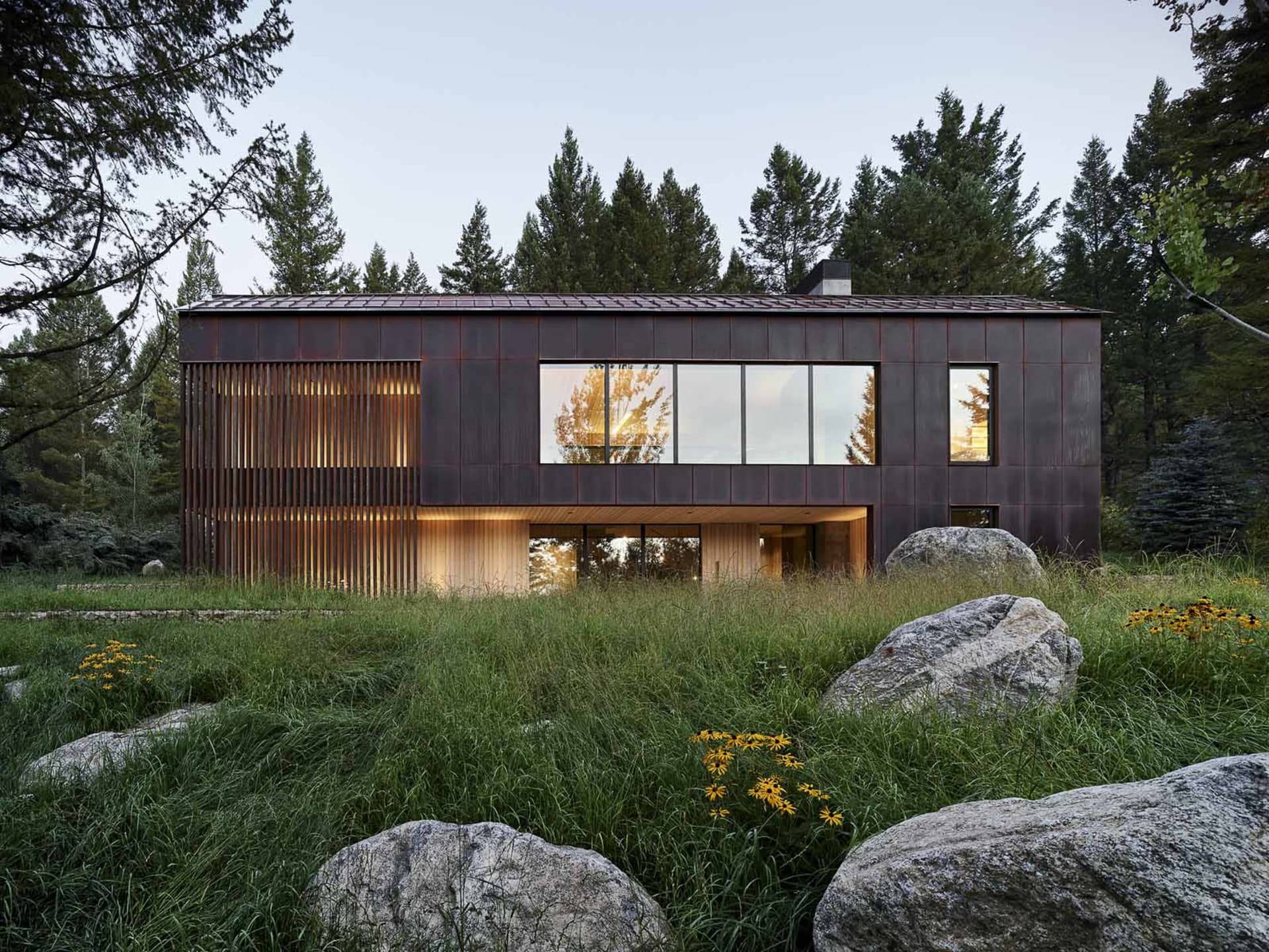 A modern metal-clad house exterior with large windows and a rustic wooden door.