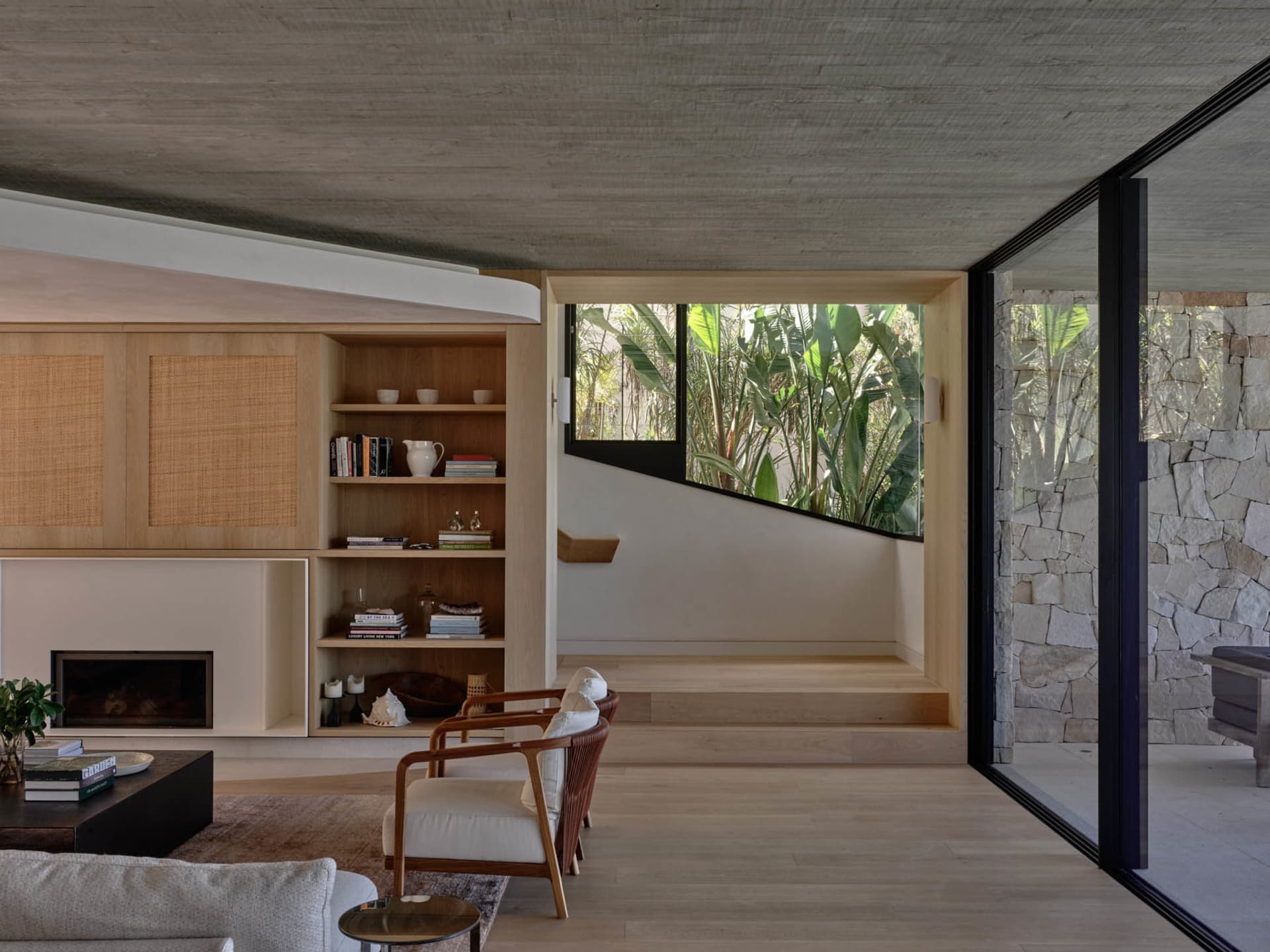 Modern, minimalist living room featuring wood furniture, concrete walls, and stone accents.