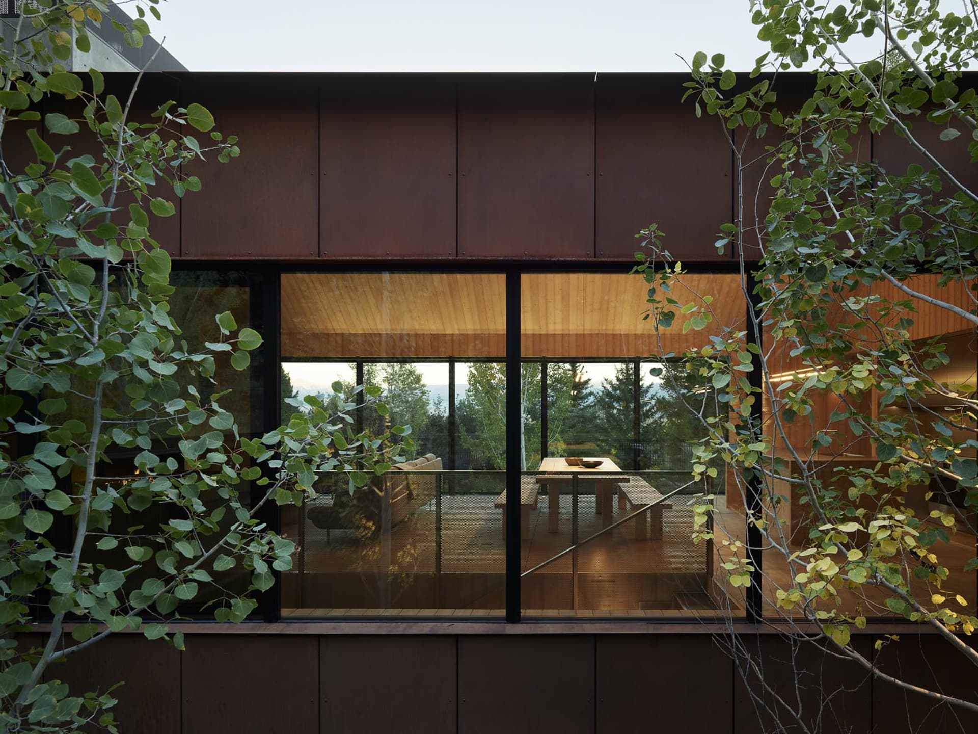 Modern residential patio area featuring wooden outdoor furniture and a metal railing.