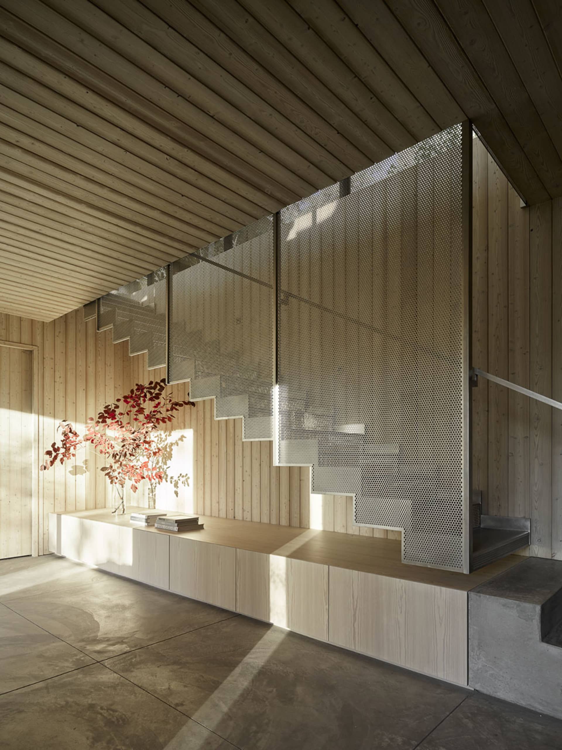A modern staircase featuring perforated metal risers, concrete treads, and wood accents alongside a minimalist interior desig