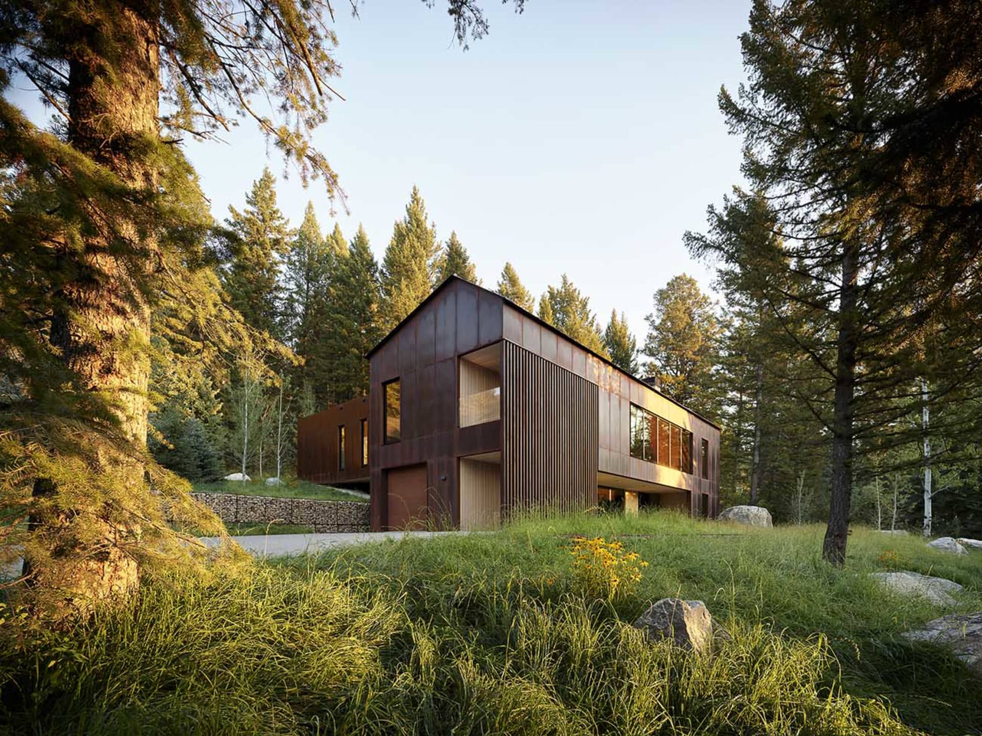 A modern, rustic house made of copper, surrounded by tall trees and greenery.