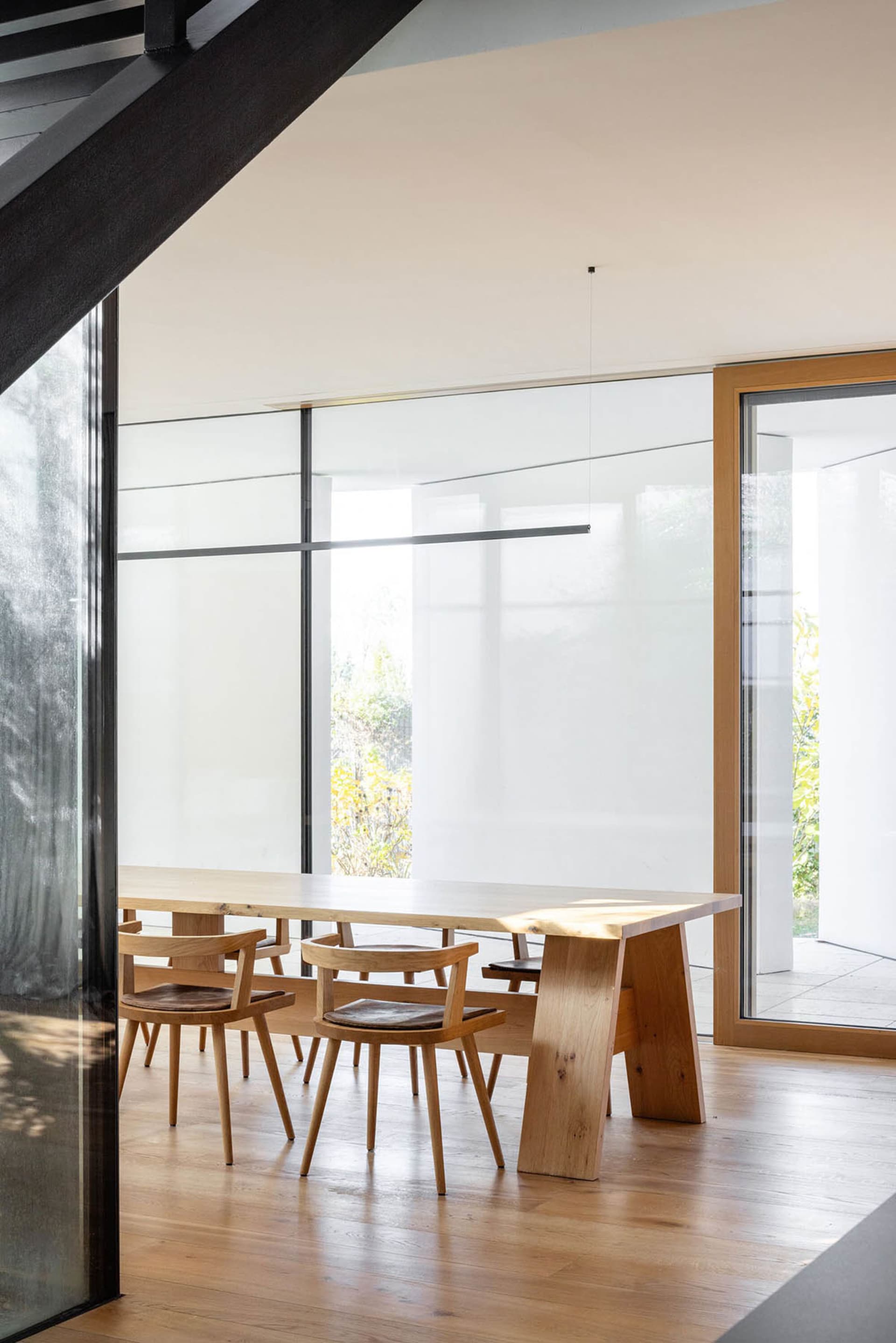 Modern minimalist living and dining area with wooden furniture and large glass windows.