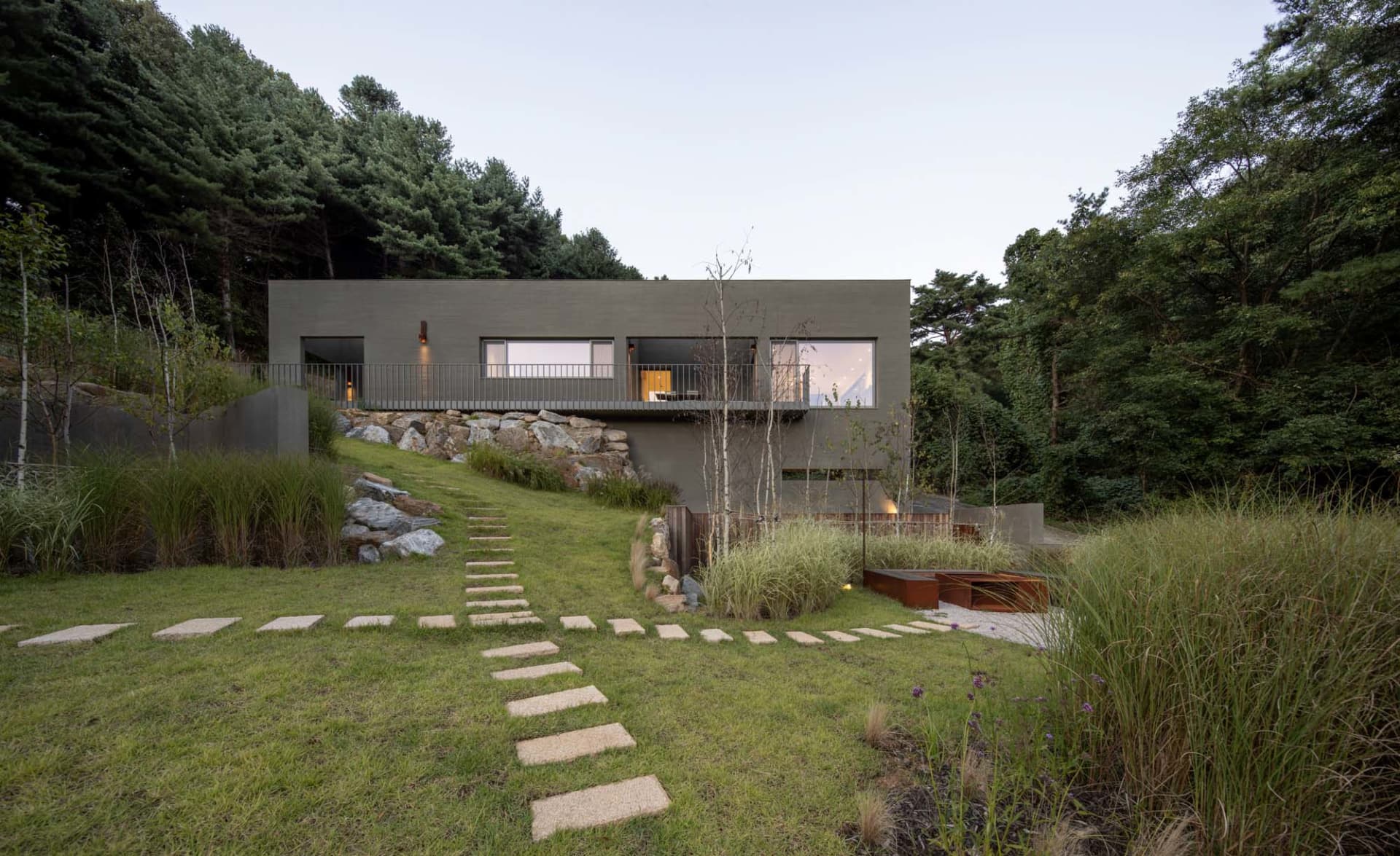 Modern residential architecture featuring a house built into a hillside with concrete and rock elements.