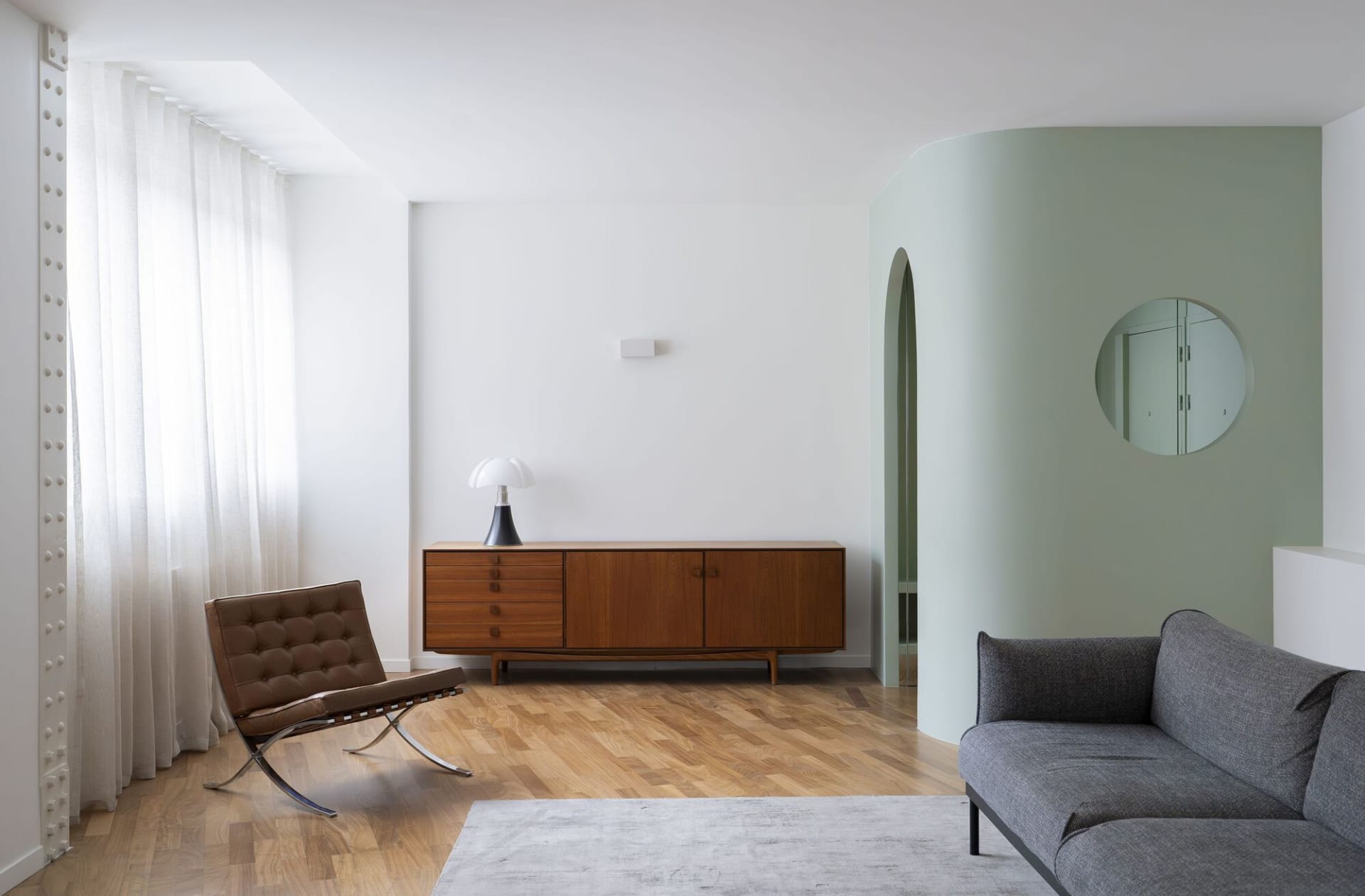 A modern minimalist living room with a leather chair, wooden cabinet, and grey sofa.