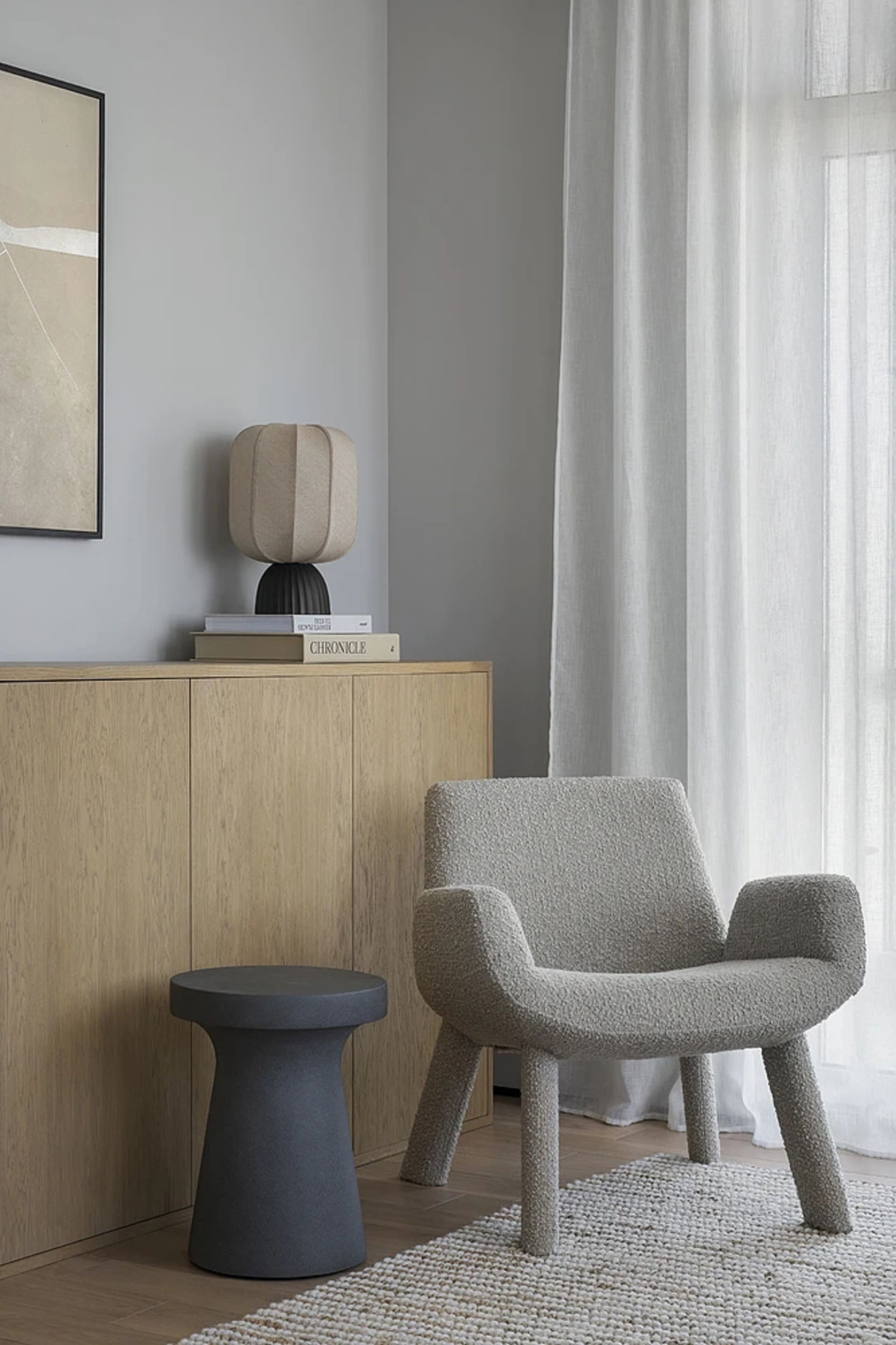 A modern living room featuring a taupe textured armchair and stool, wooden sideboard, and neutral color palette.