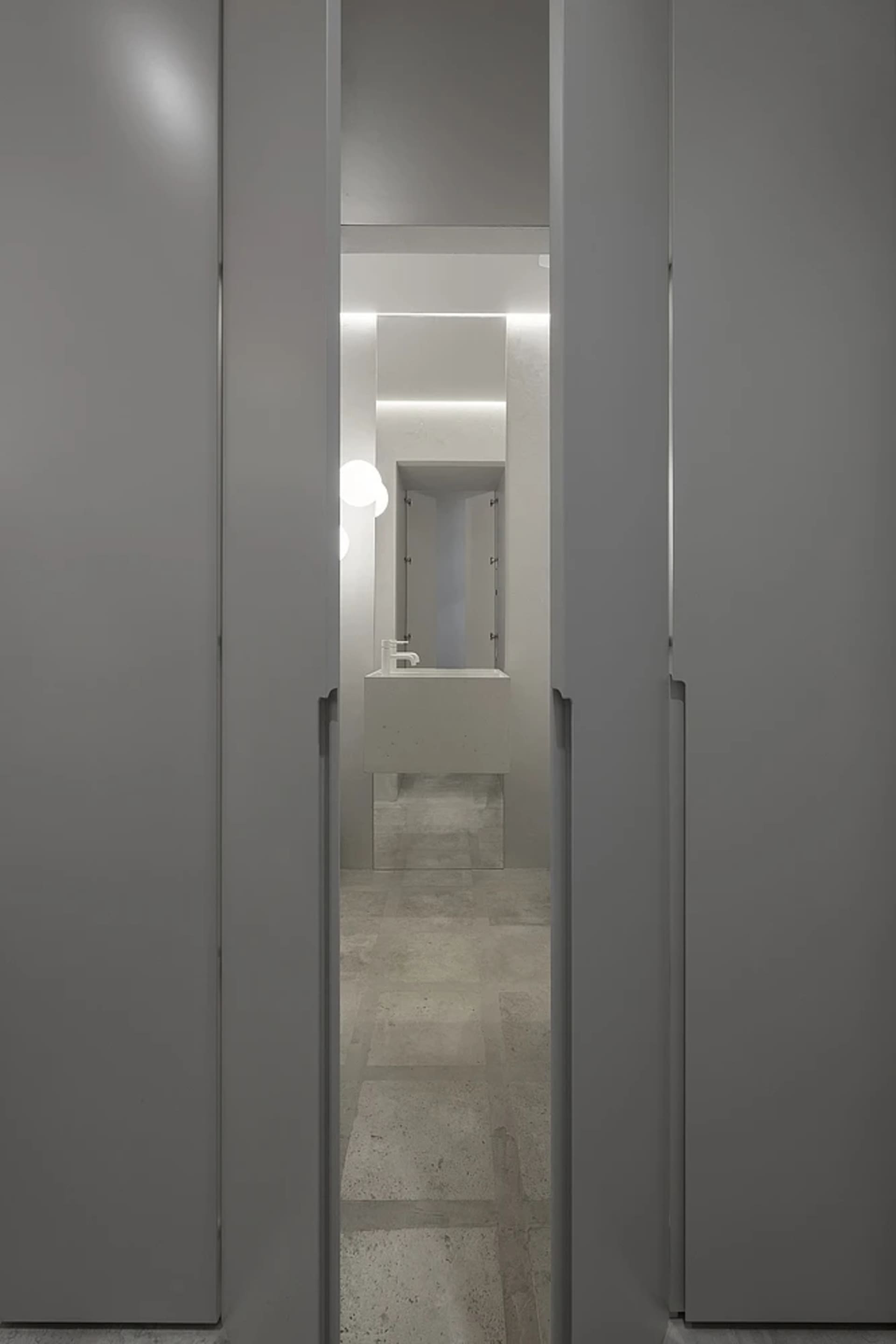 A minimalist bathroom featuring a modern concrete sink and floor, with a small mirror and light fixture.