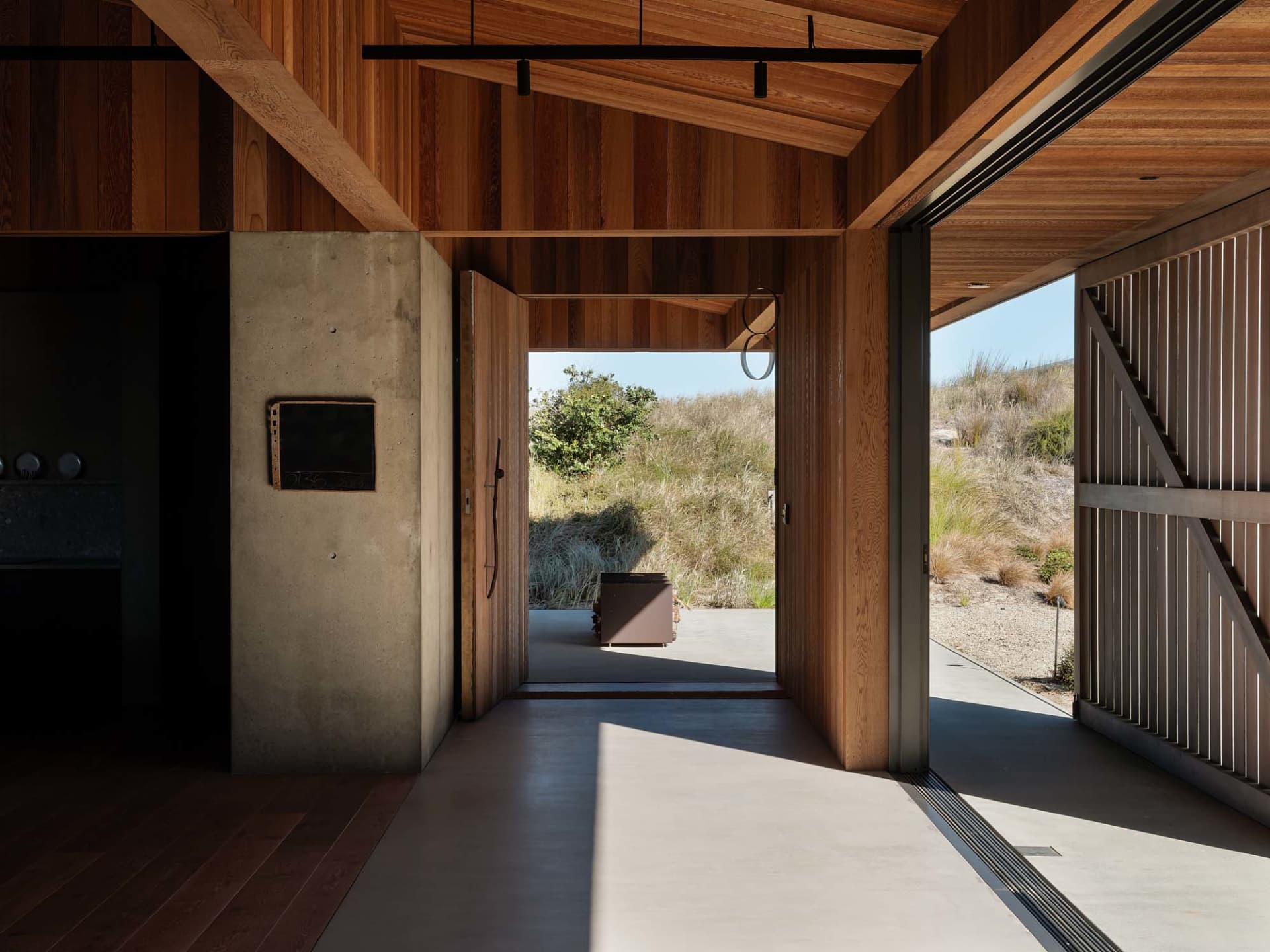 An open-plan minimalist entryway with wooden walls, floor, and ceiling, featuring a concrete partition and a view of the natu