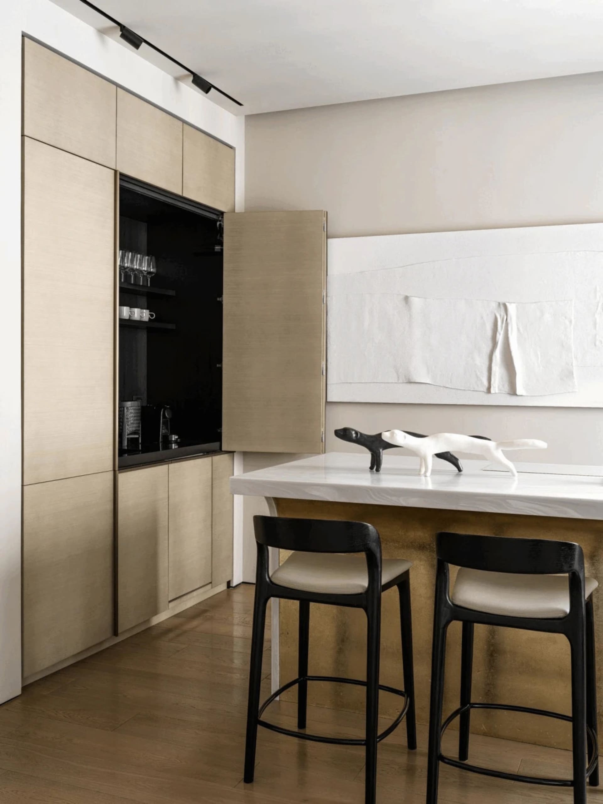 A modern minimalist kitchen with a wooden cabinet and island, white countertop, and black stools.