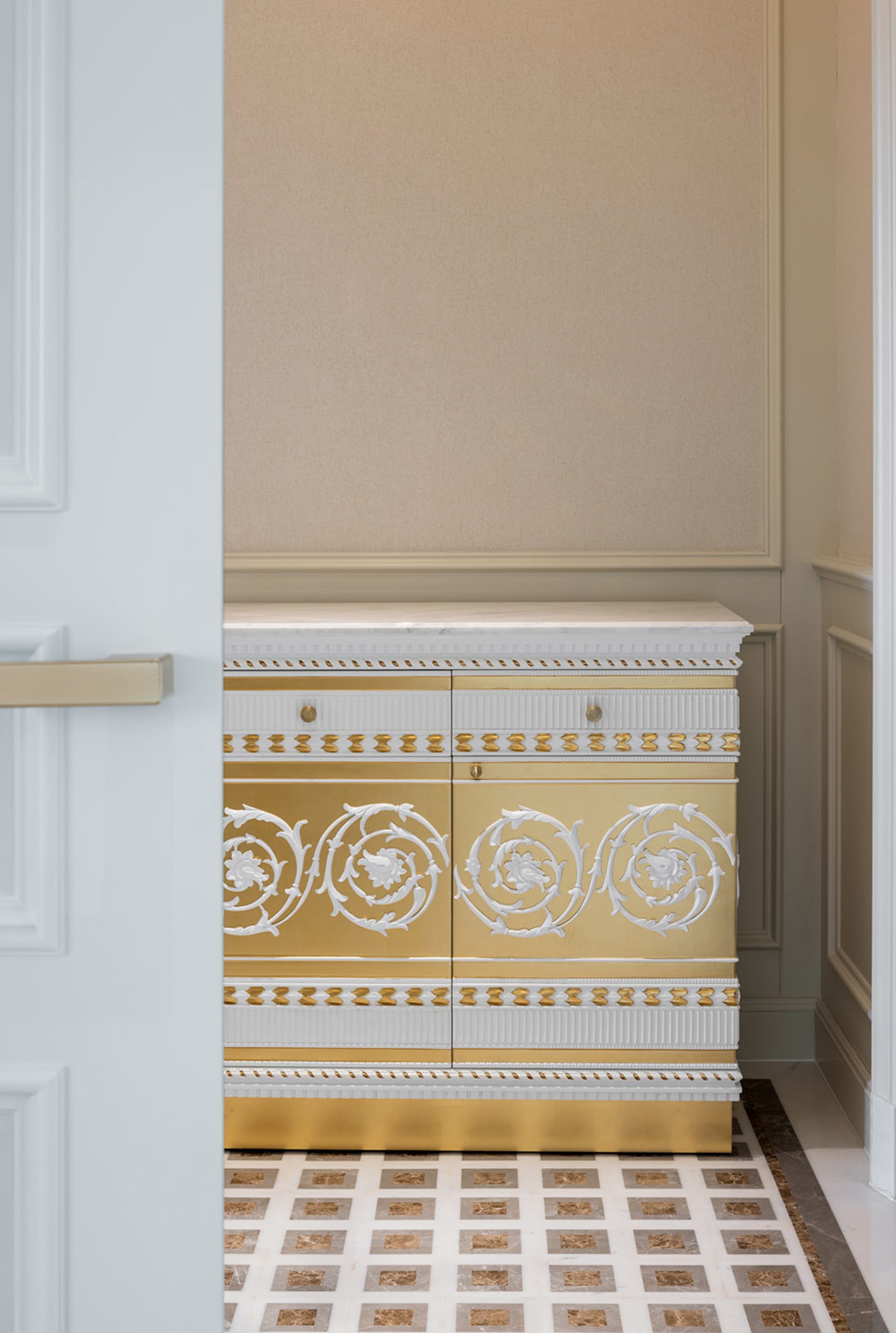 A gold and white dresser with intricate designs in a well-lit interior space.