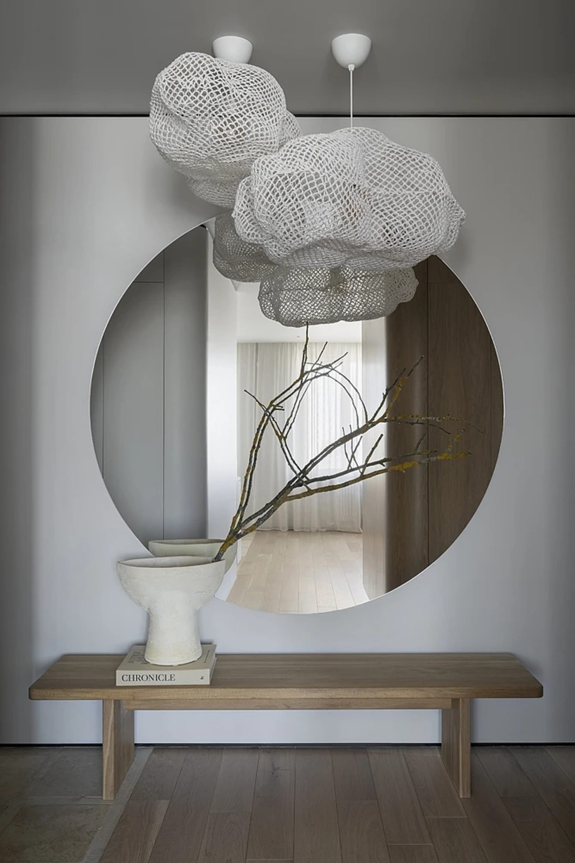 Modern minimalist entryway decorated with airy, white cloud-like lighting fixtures, a round mirror reflecting a serene interi