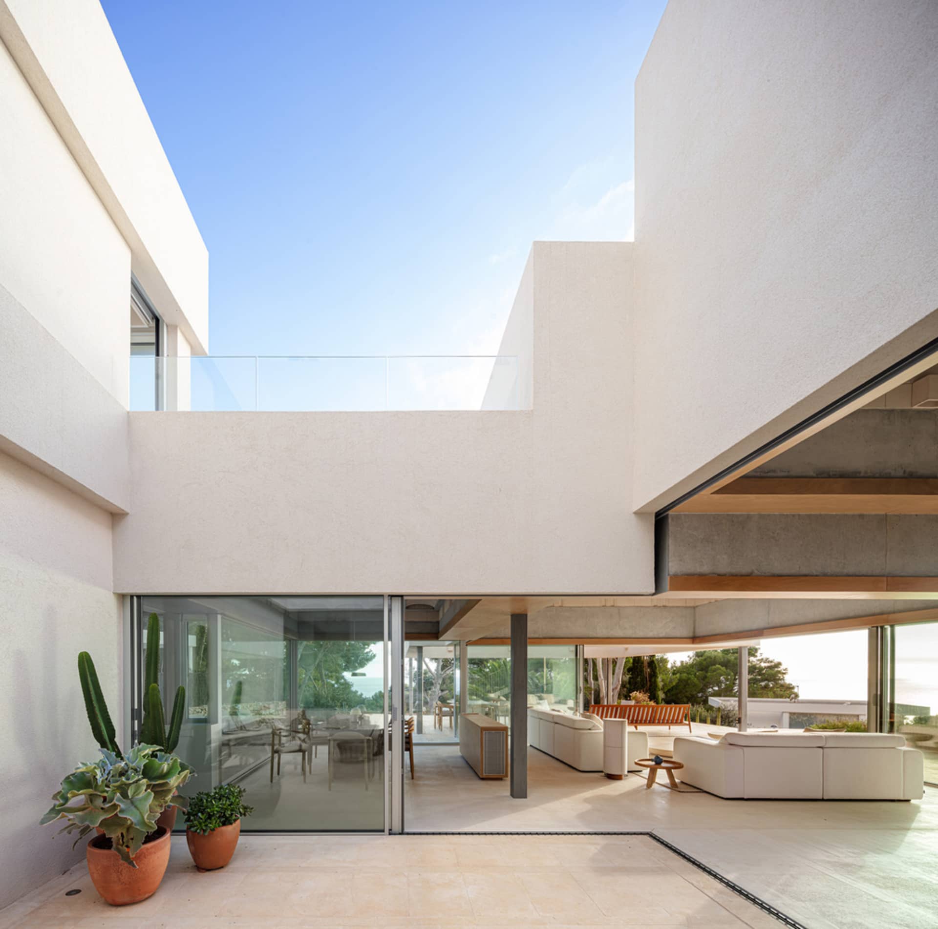 A modern, minimalist patio area with white concrete walls and floors, featuring a glass balcony and large open space with sea