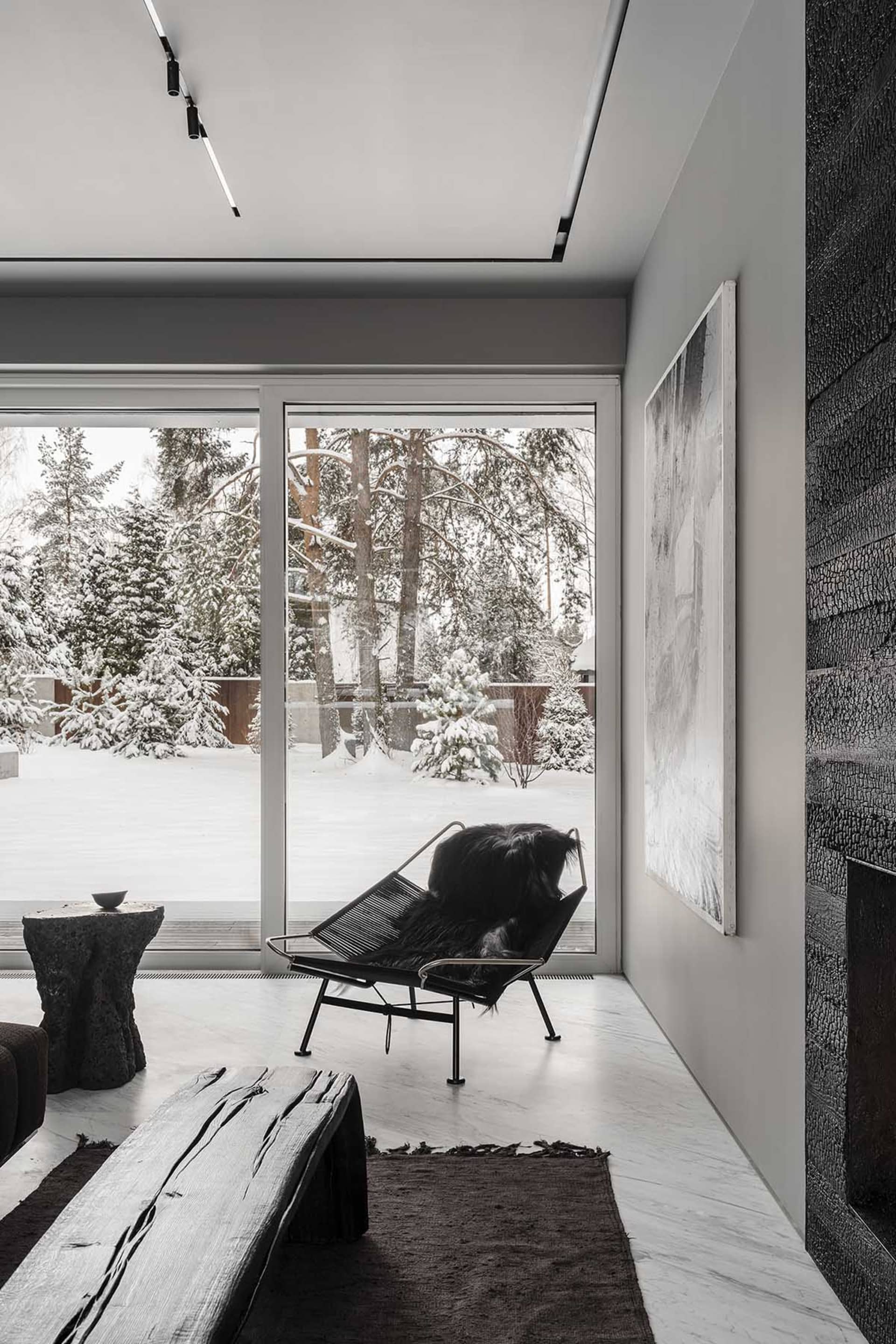Modern living room with a view of a snowy cityscape, featuring a black lounge chair with a fur blanket, a wooden bench, and a