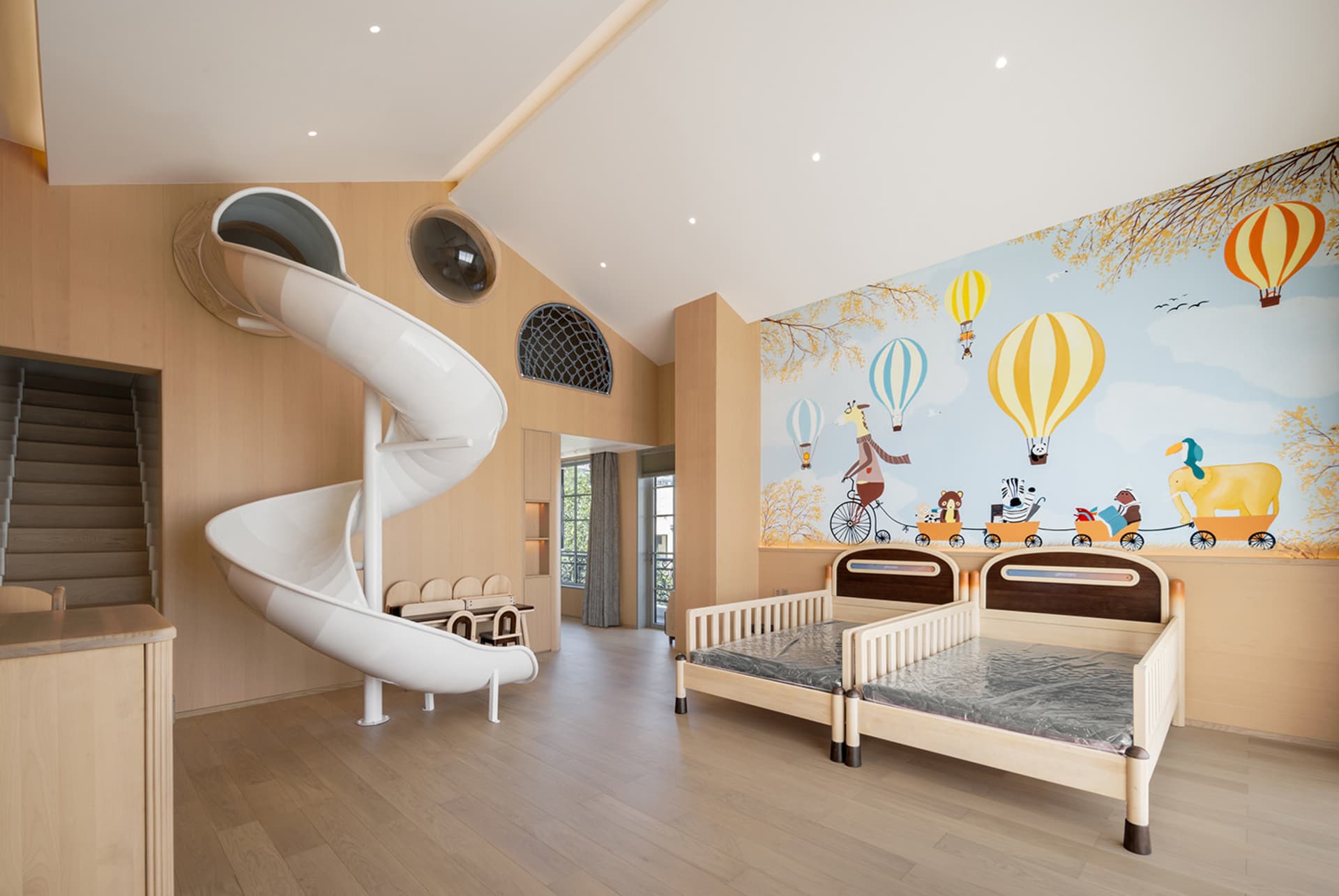 A children's room featuring a wooden slide and beds with a mural of hot air balloons and animals on the wall.