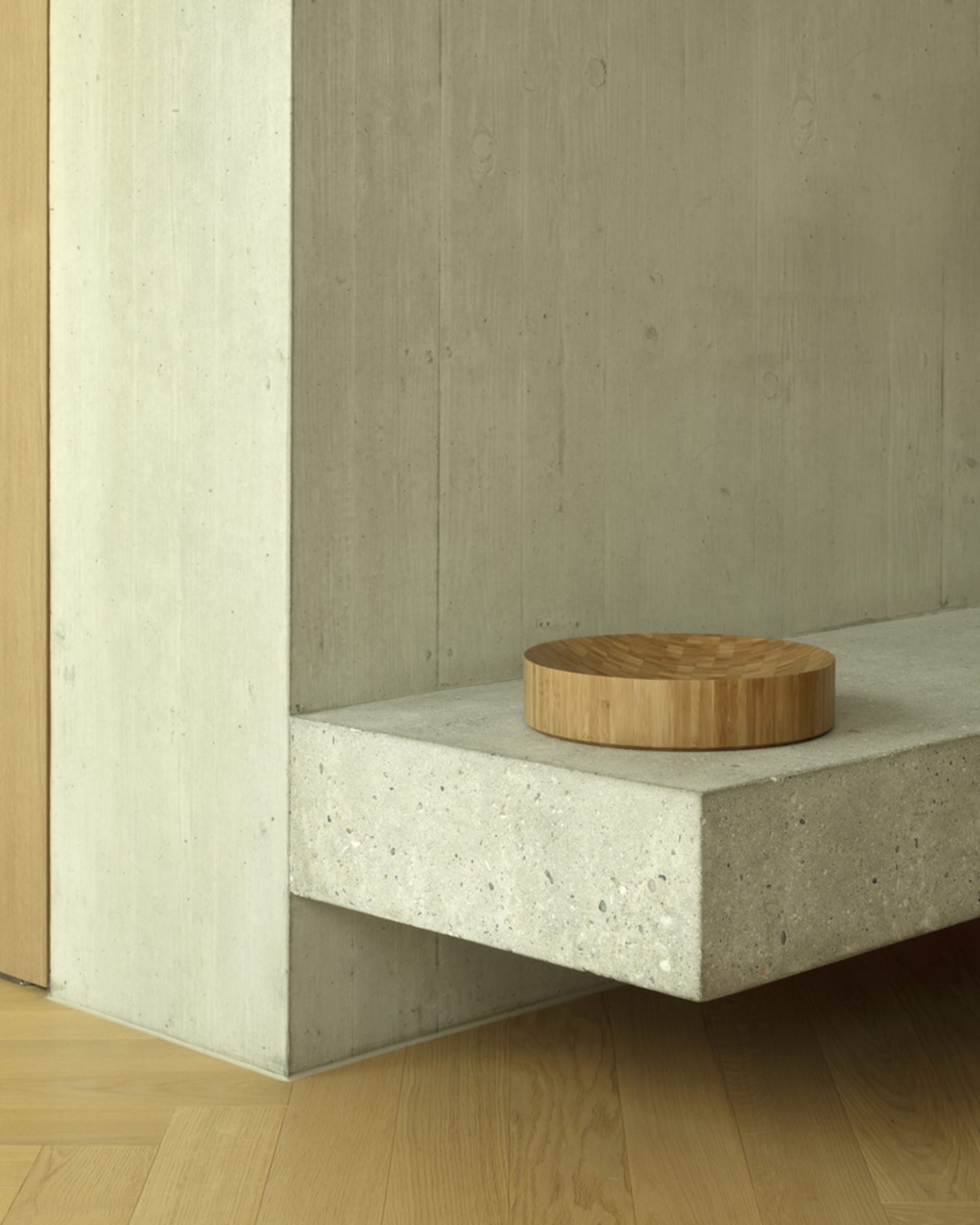 A minimalist interior design featuring a concrete shelf with a circular wooden object on it.