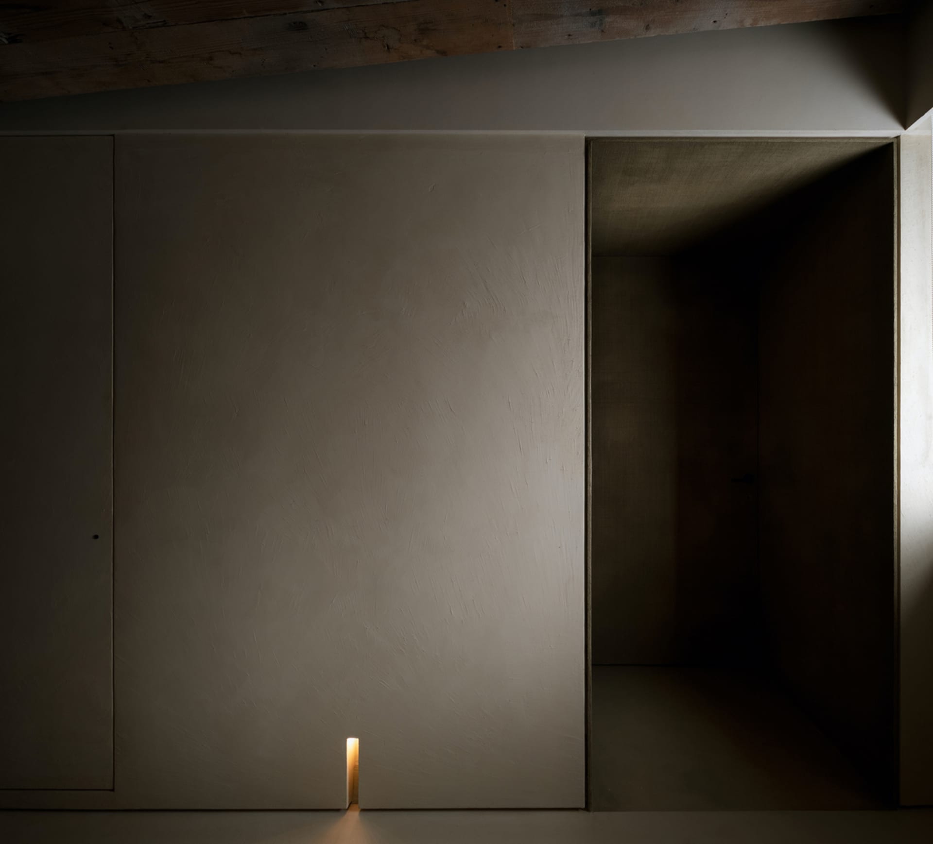 An interior space with a minimalist design featuring a concrete wall and doorway.