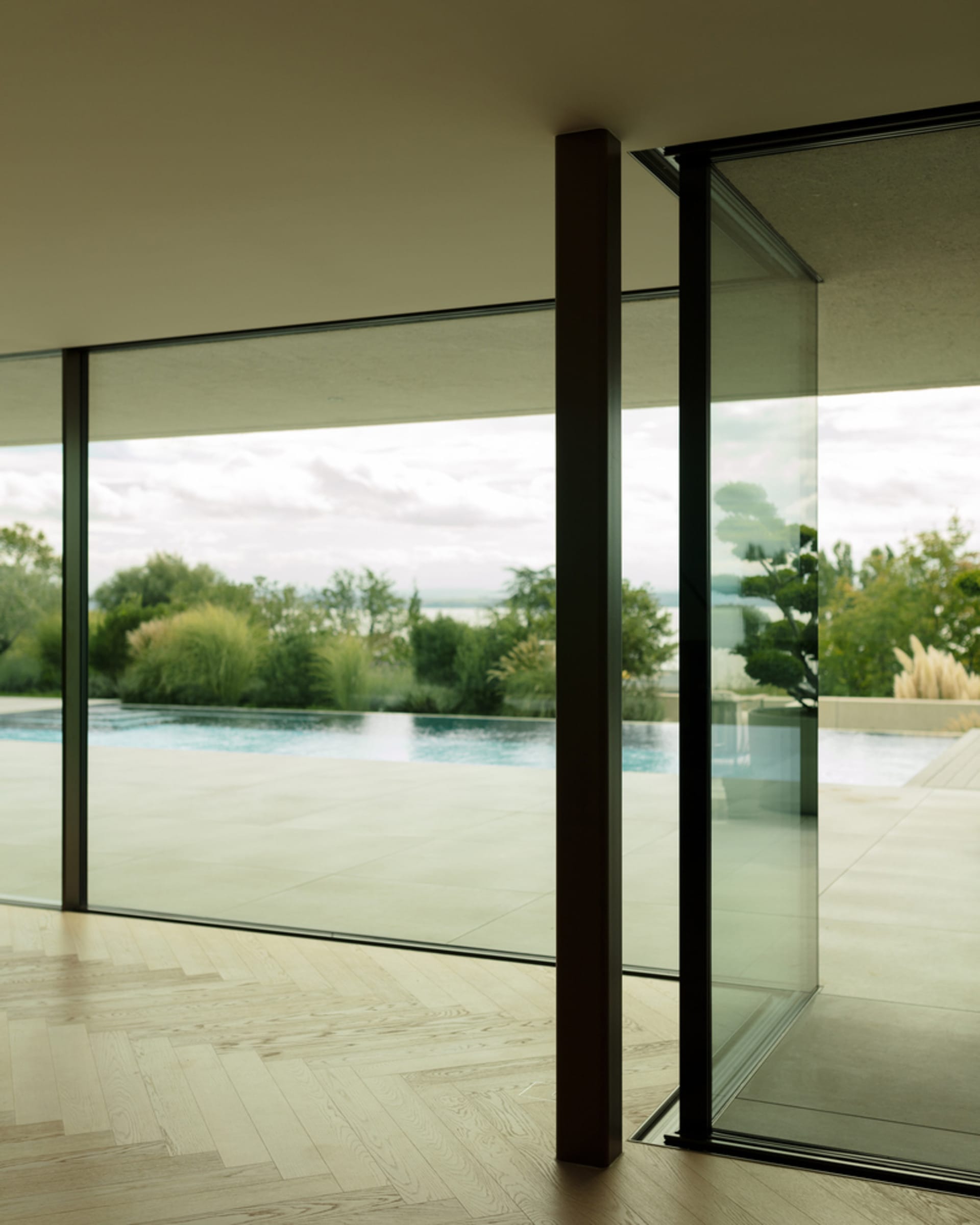 A modern glass window overlooking a serene outdoor space and pool, framed by minimal interior design.