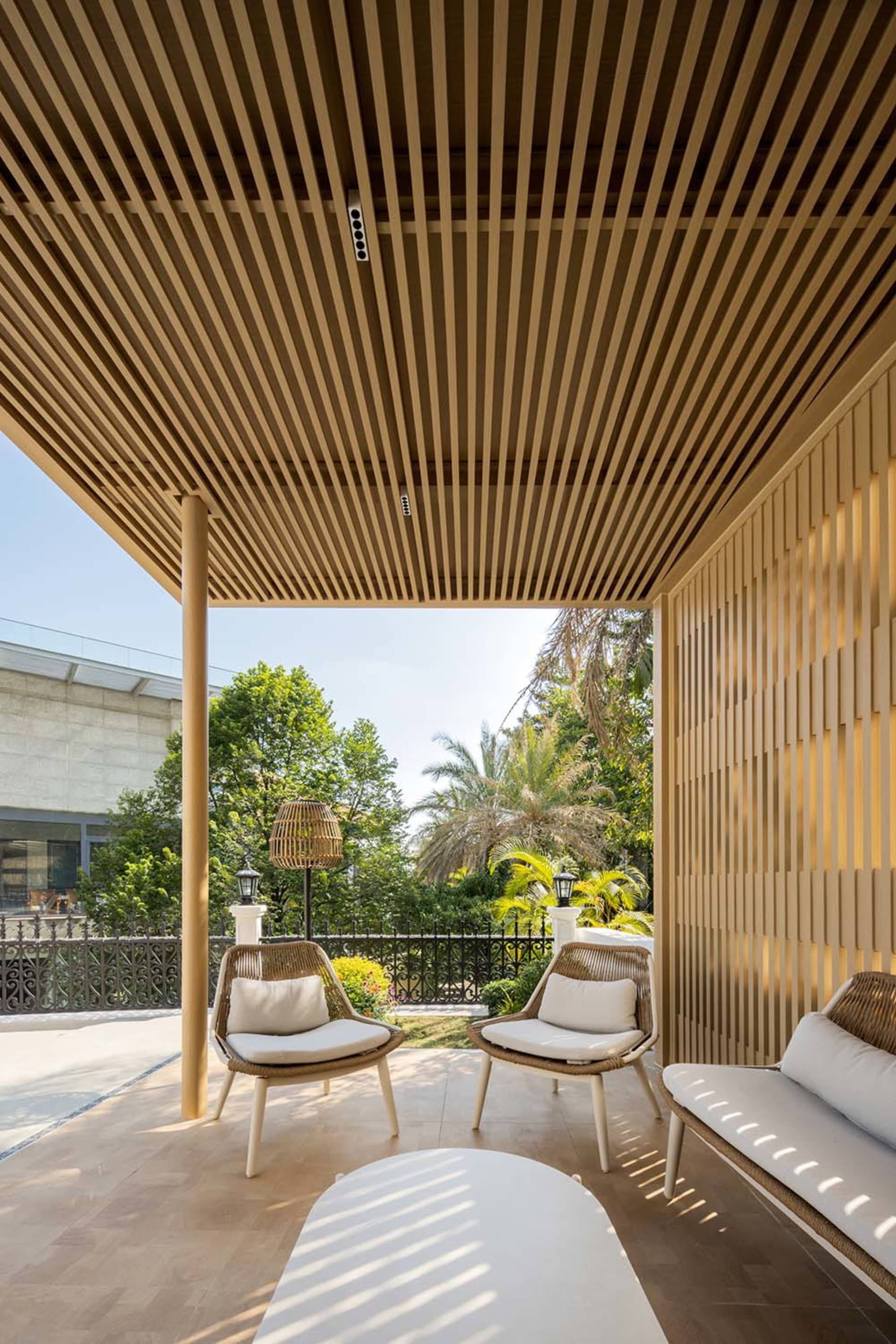 A residential patio with wooden slats, featuring outdoor furniture and a view of greenery.