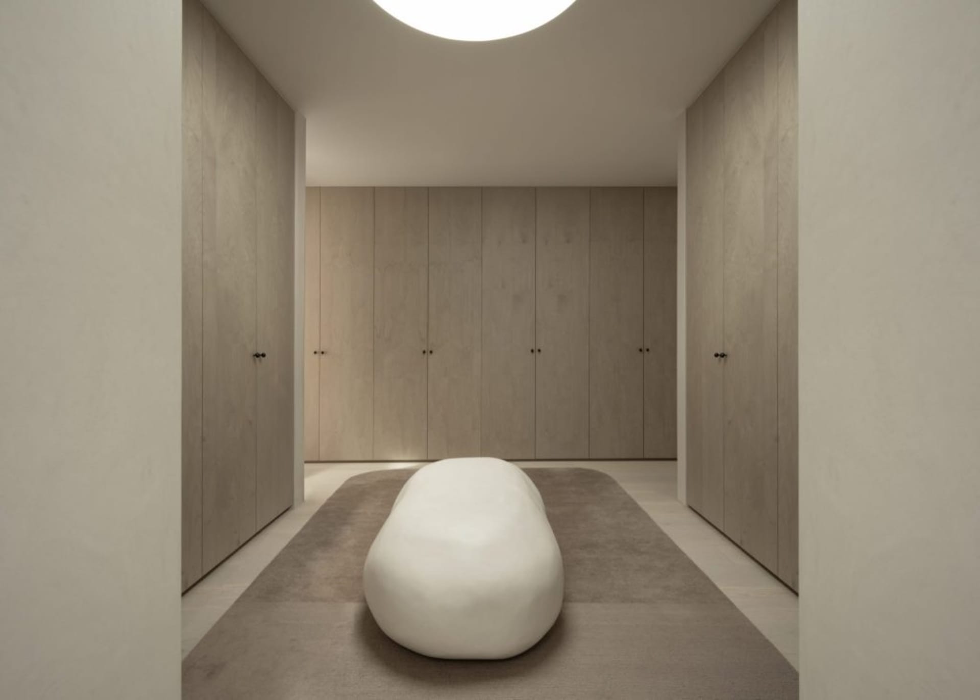 A minimalist bedroom with neutral tones and a sculptural white bench.