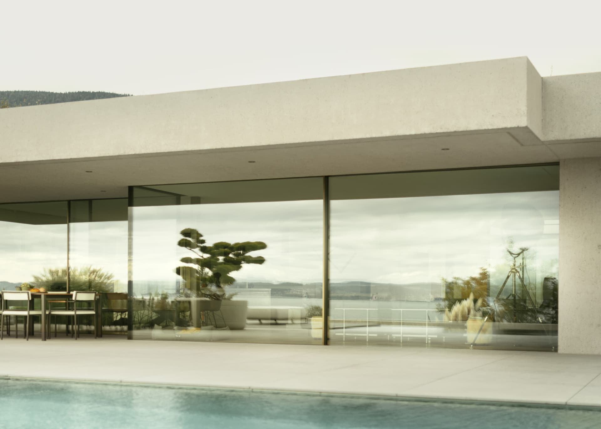A modern residential exterior featuring a large glass wall overlooking a serene water body and distant hills.