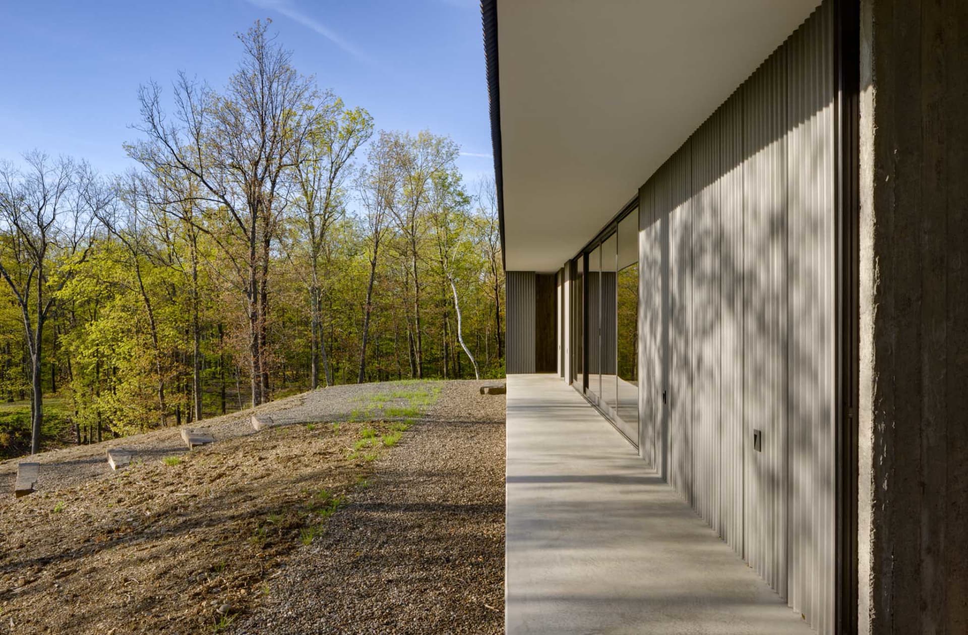 Modern residential building exterior with metal siding and large windows overlooking a forested area.