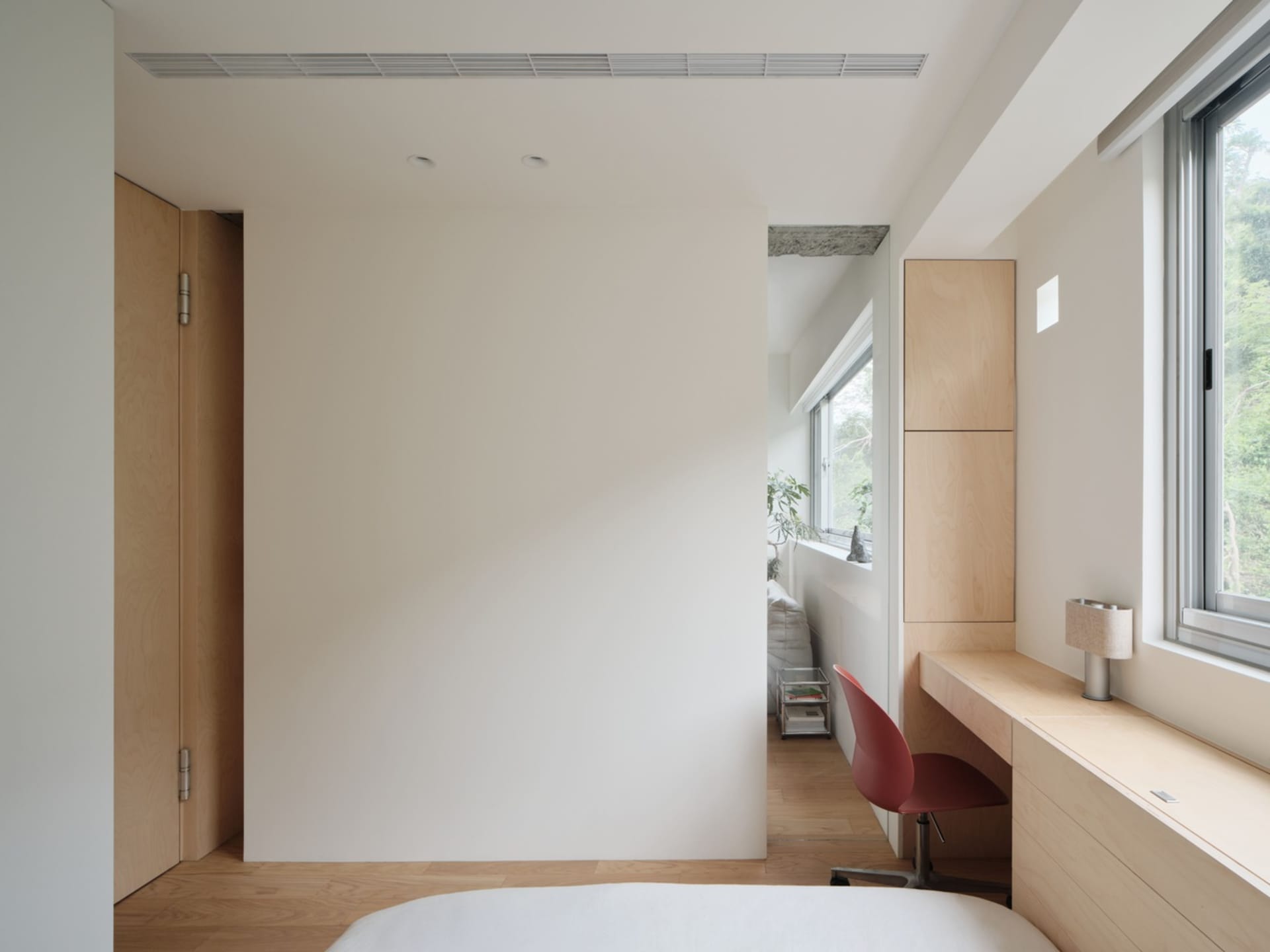 A minimalist bedroom featuring wooden furniture, white walls, and a red desk chair.