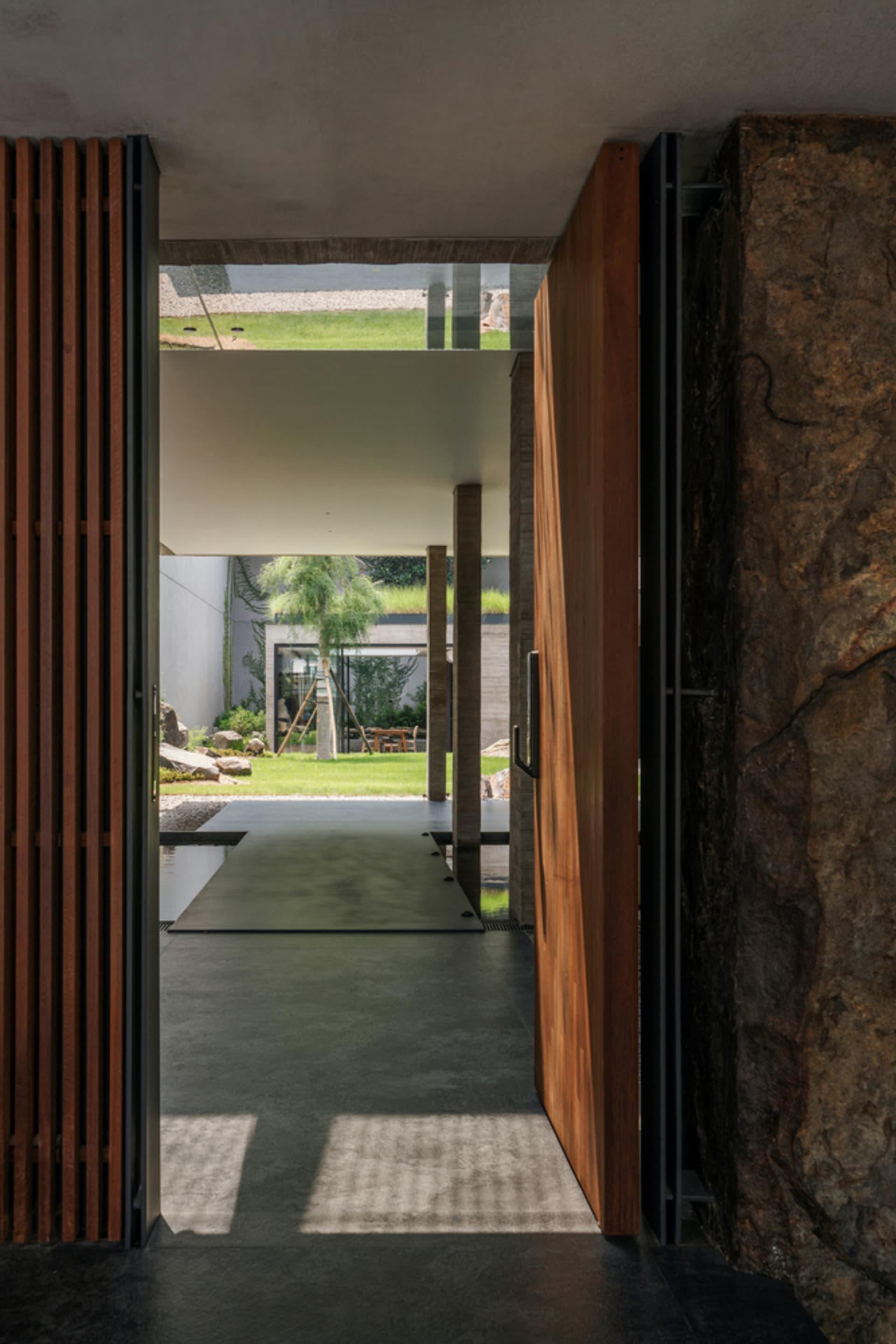 A modern entrance hall with wooden doors, concrete flooring, and a stone wall.