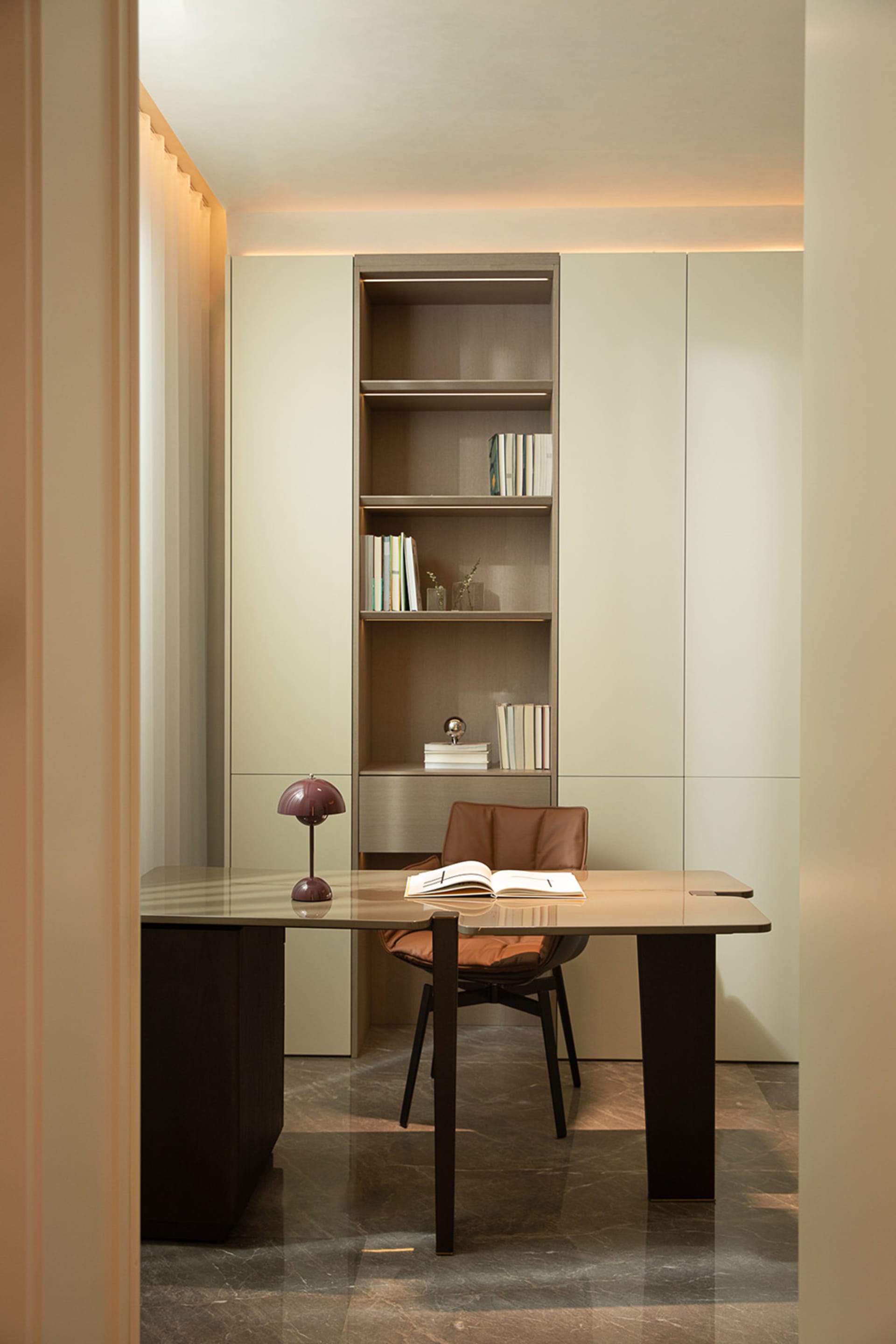 A modern home office with a sleek desk, leather chair, wooden bookshelf, and minimalist interior design.