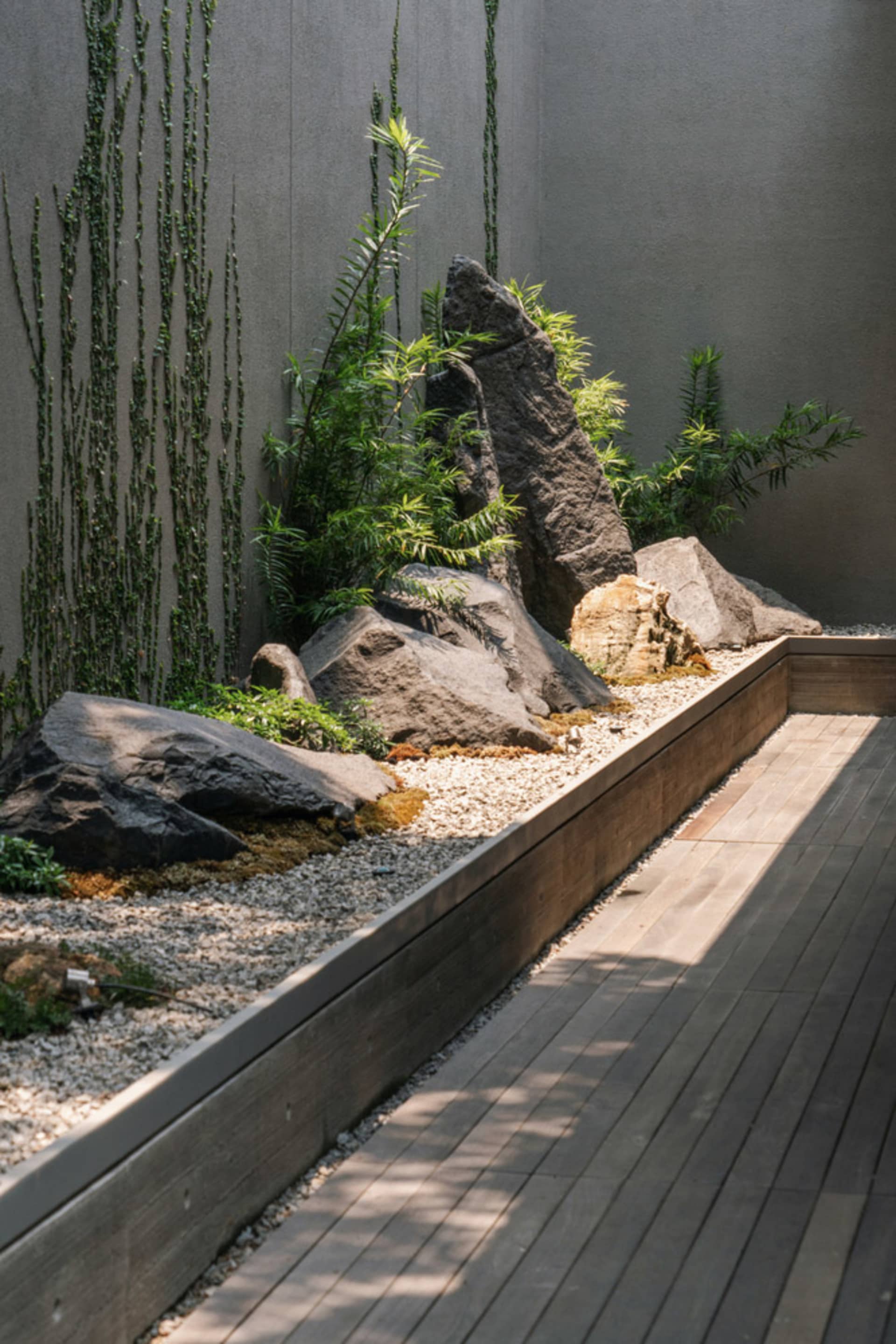 現代石園，巨石與綠植映襯混凝土牆，前景為木質平台。