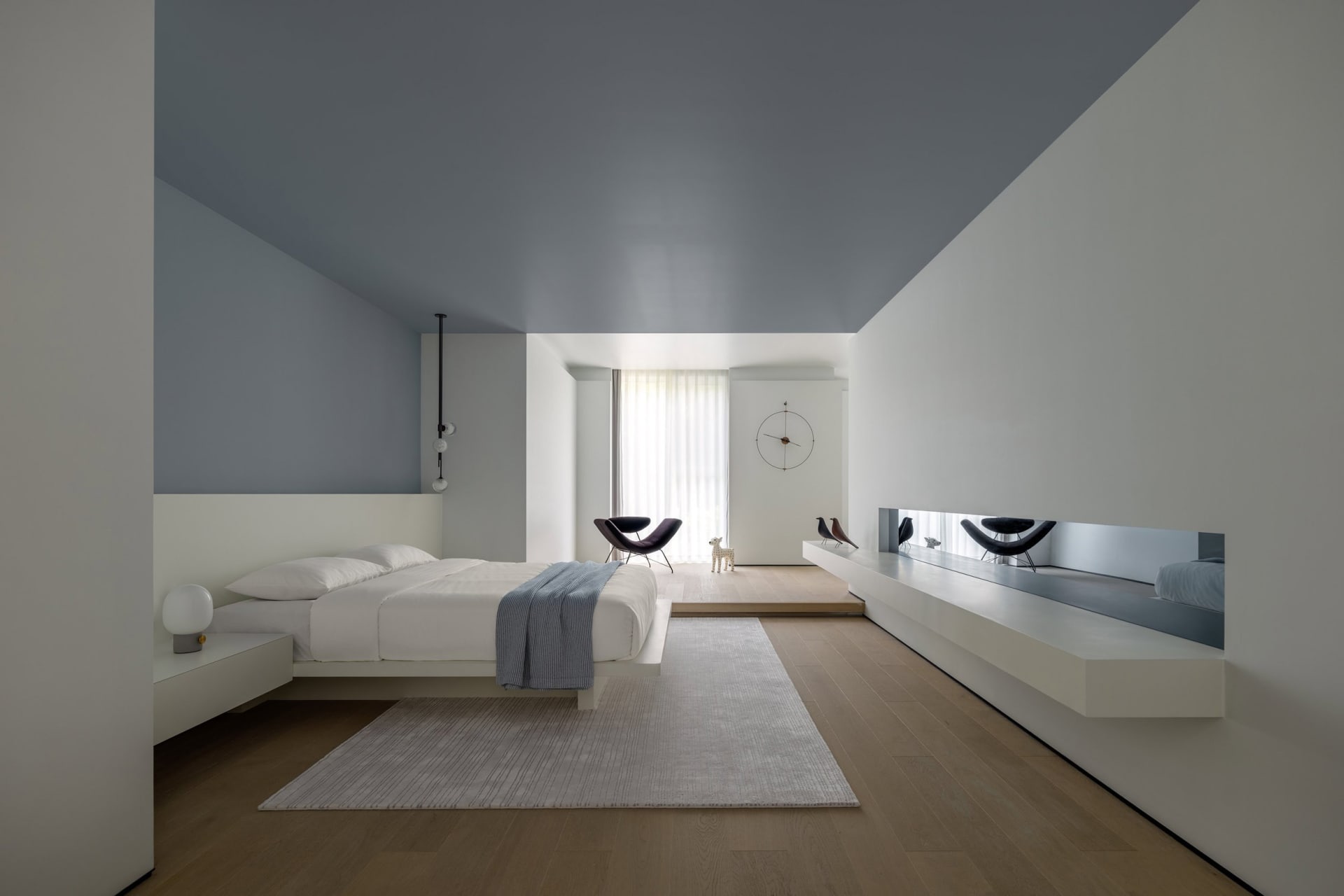 A modern minimalist bedroom with concrete surfaces, featuring a low bed platform, floating nightstands, and a sleek, contempo