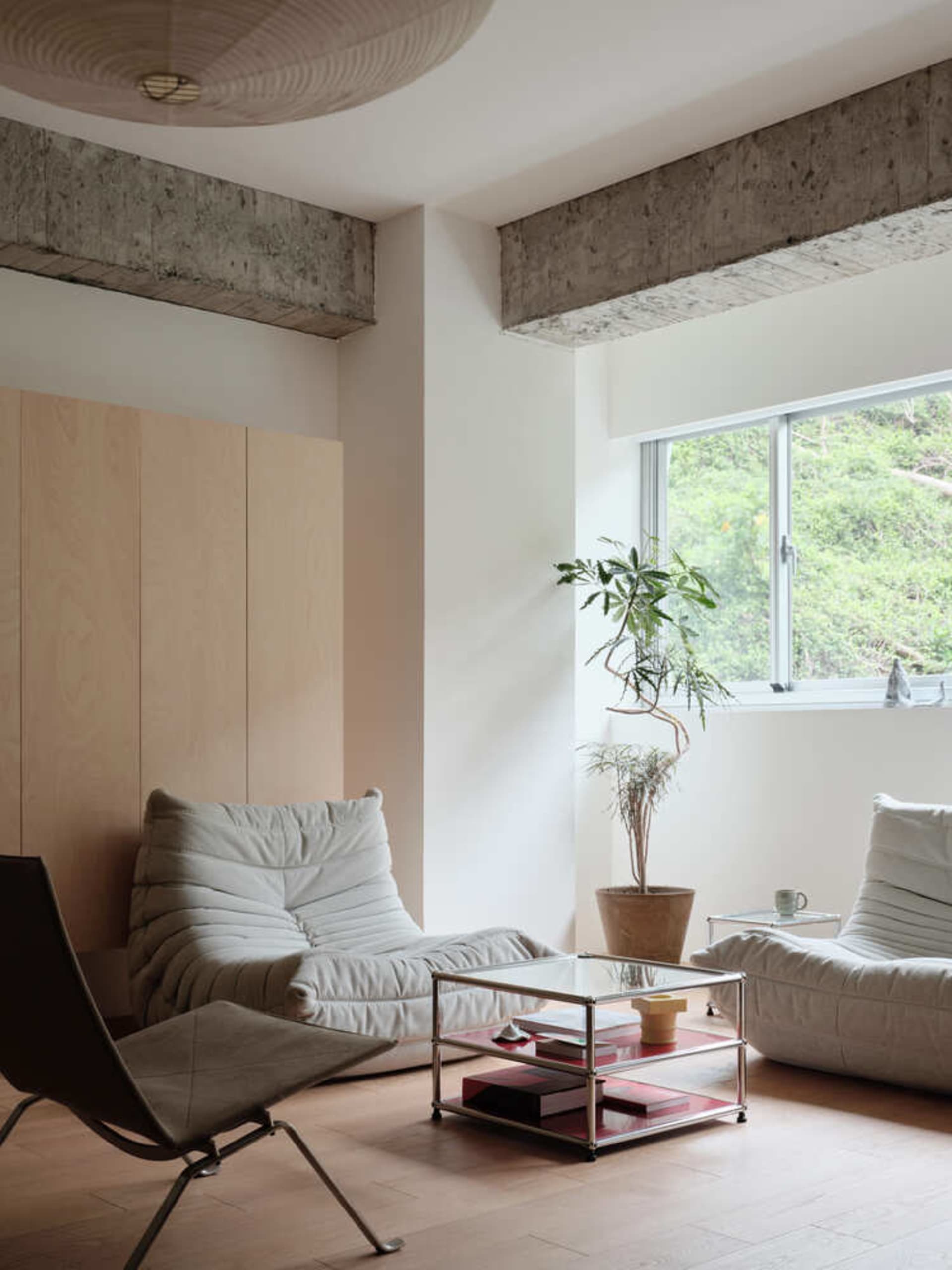 A modern minimalist living room features white sofas, a glass coffee table, and plant accents against a concrete ceiling and