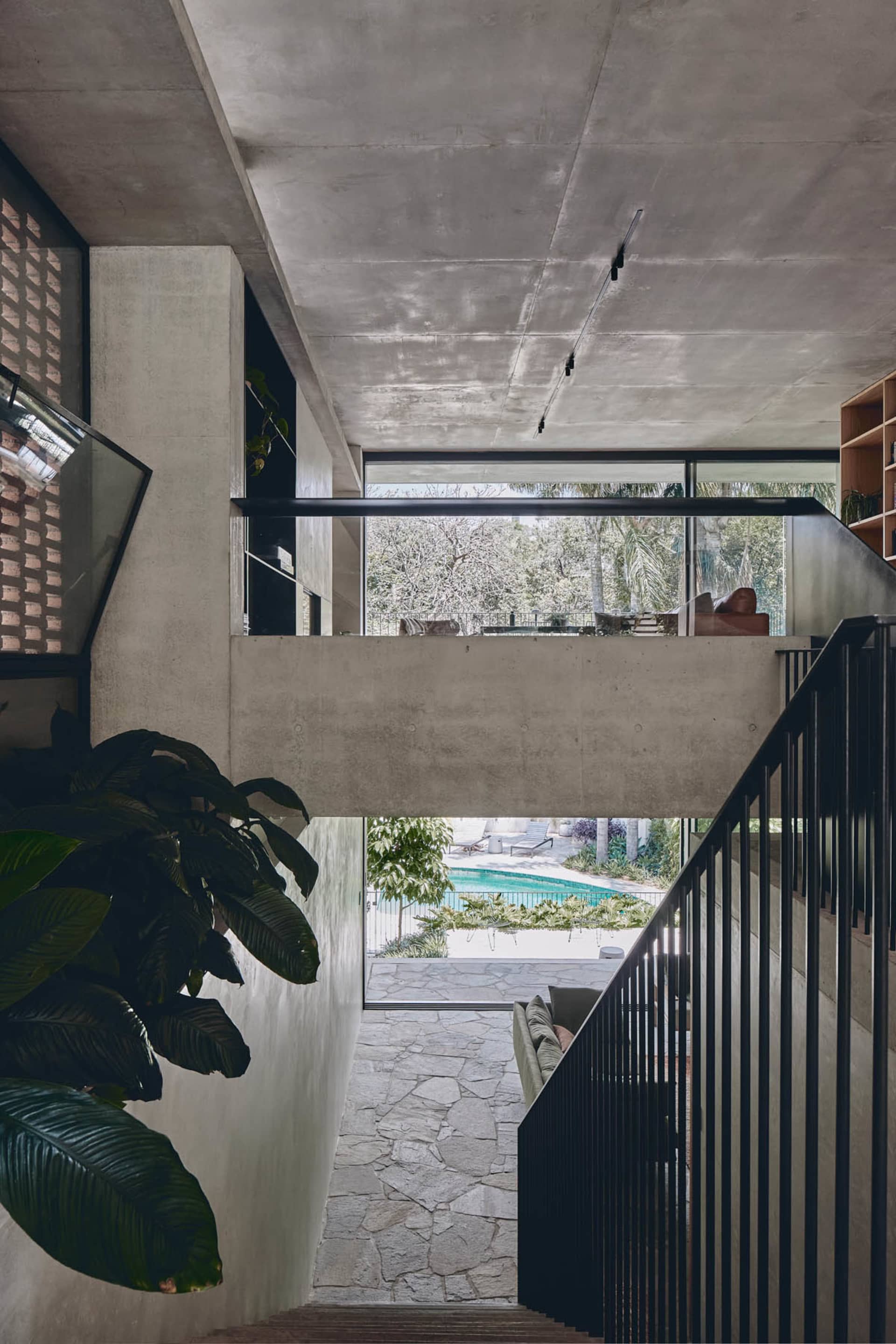 A modern house interior featuring a concrete staircase with a black railing, leading to a living area with natural light and