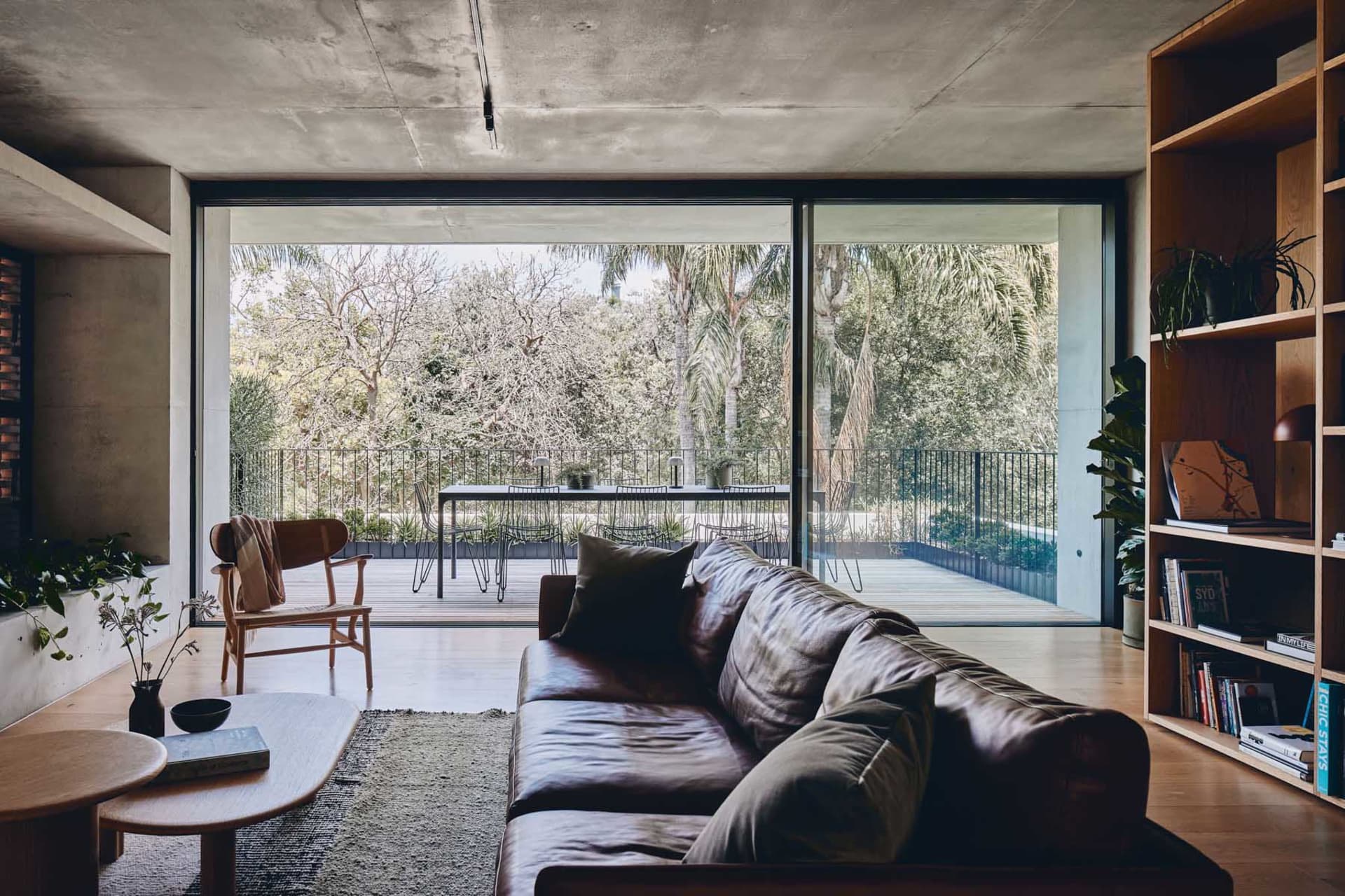 A modern living room featuring a concrete ceiling, a leather sofa, a wooden coffee table, and a bookshelf filled with books a