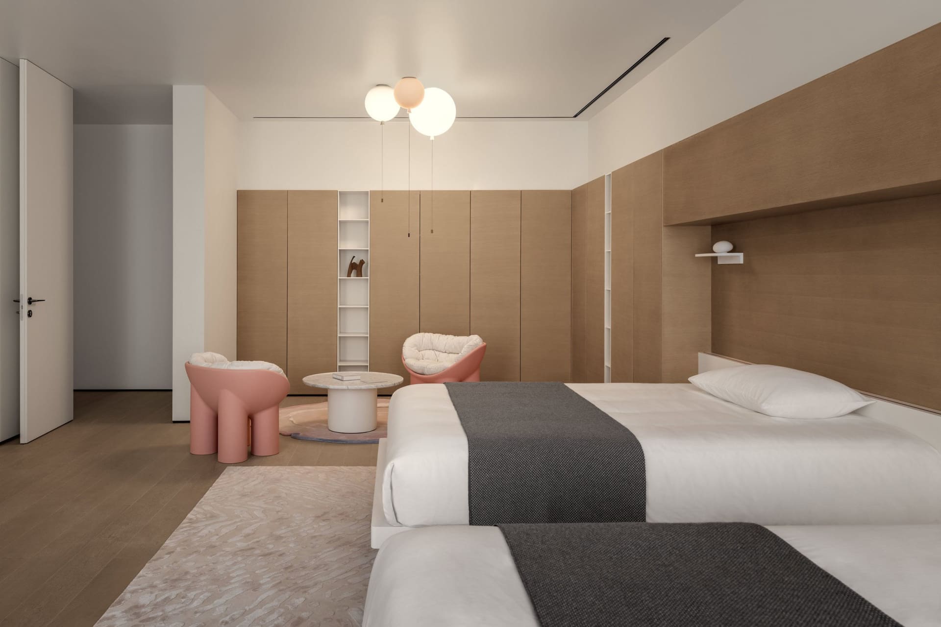 Modern minimalist bedroom with wooden walls and built-in cabinets, featuring a pink accent chair and table, and a comfortable
