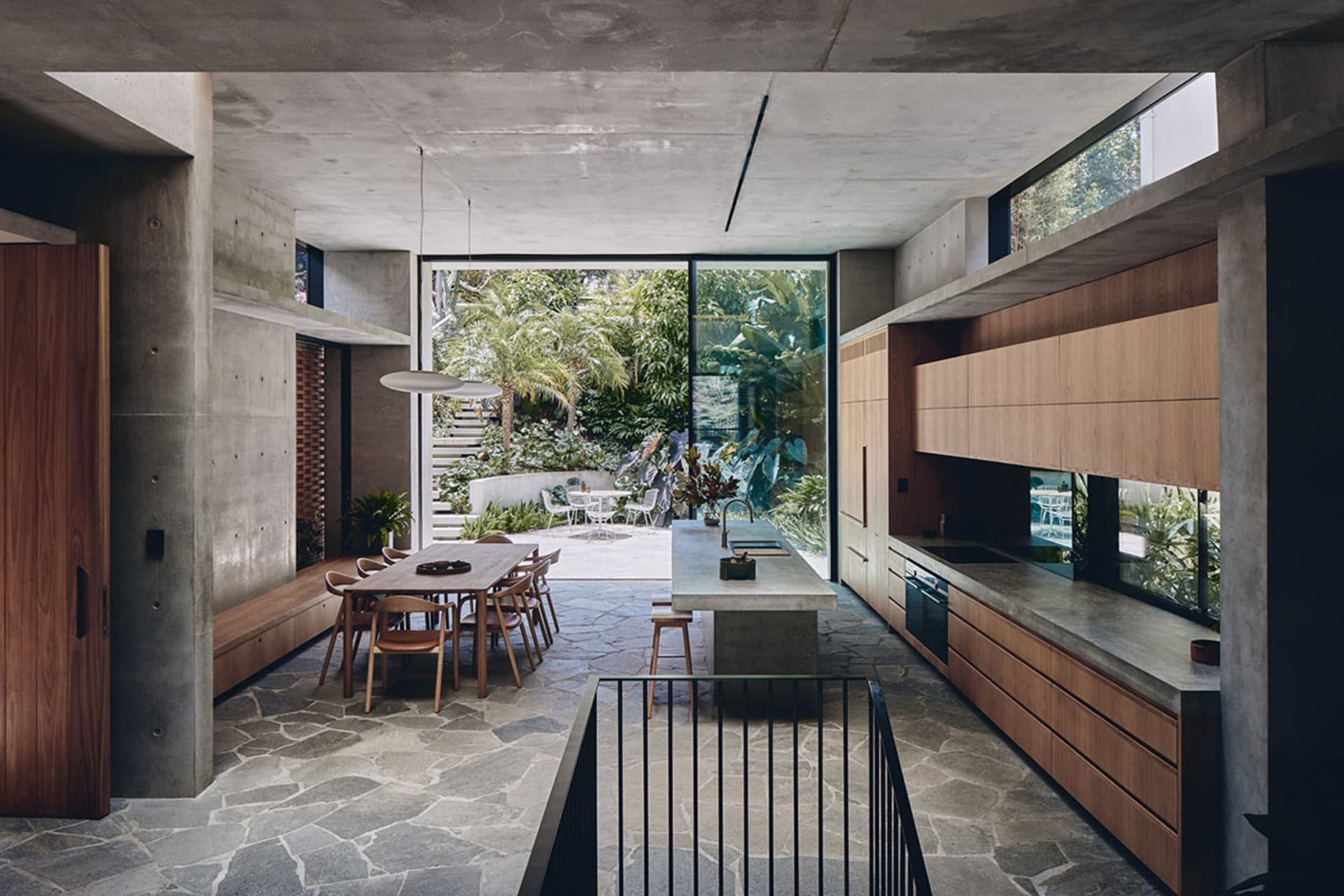 Modern residential kitchen featuring a concrete floor, wooden cabinets, and a large window overlooking a garden.