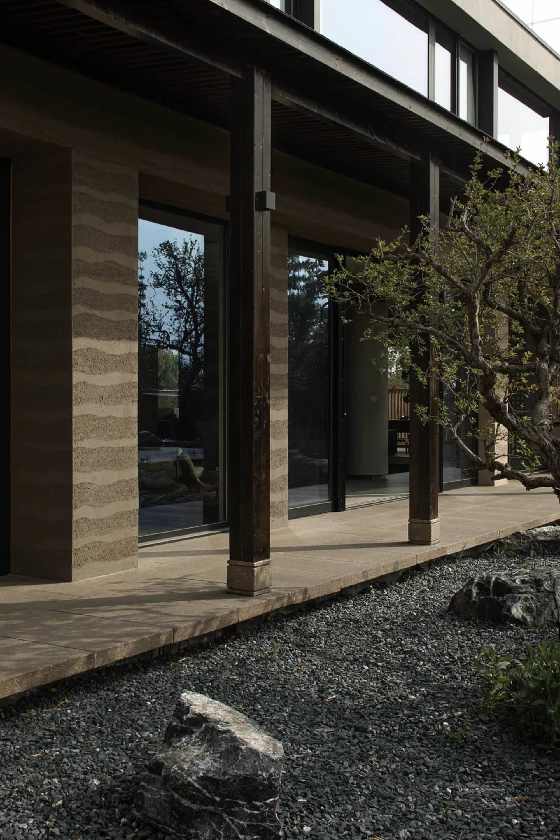 Modern house exterior with concrete and wooden columns and a gravel garden with rocks and plants.
