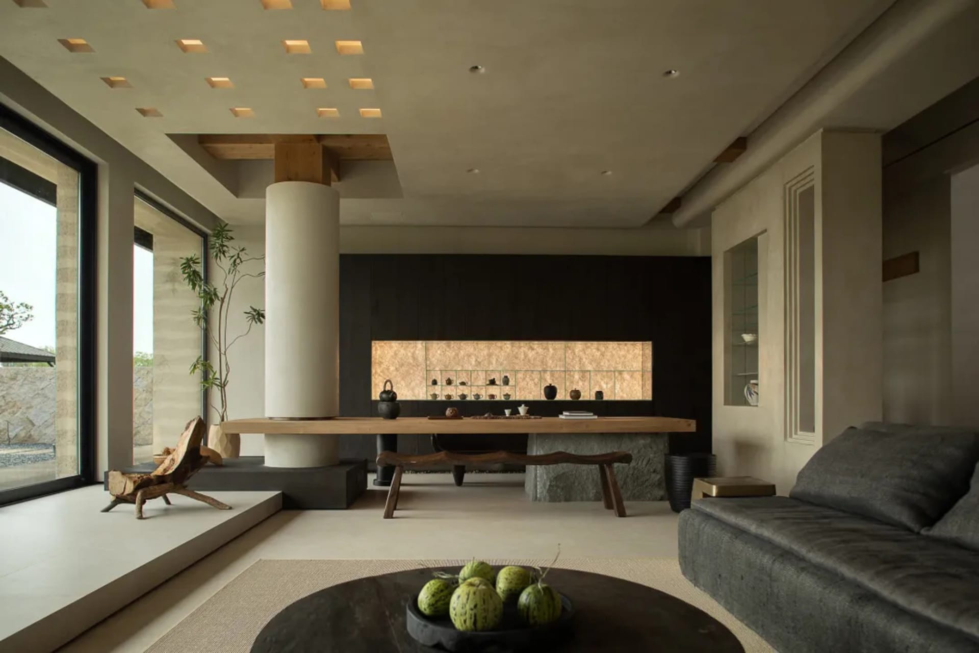 Modern living room with exposed concrete ceiling and walls, featuring a large table with vases and potted plants.