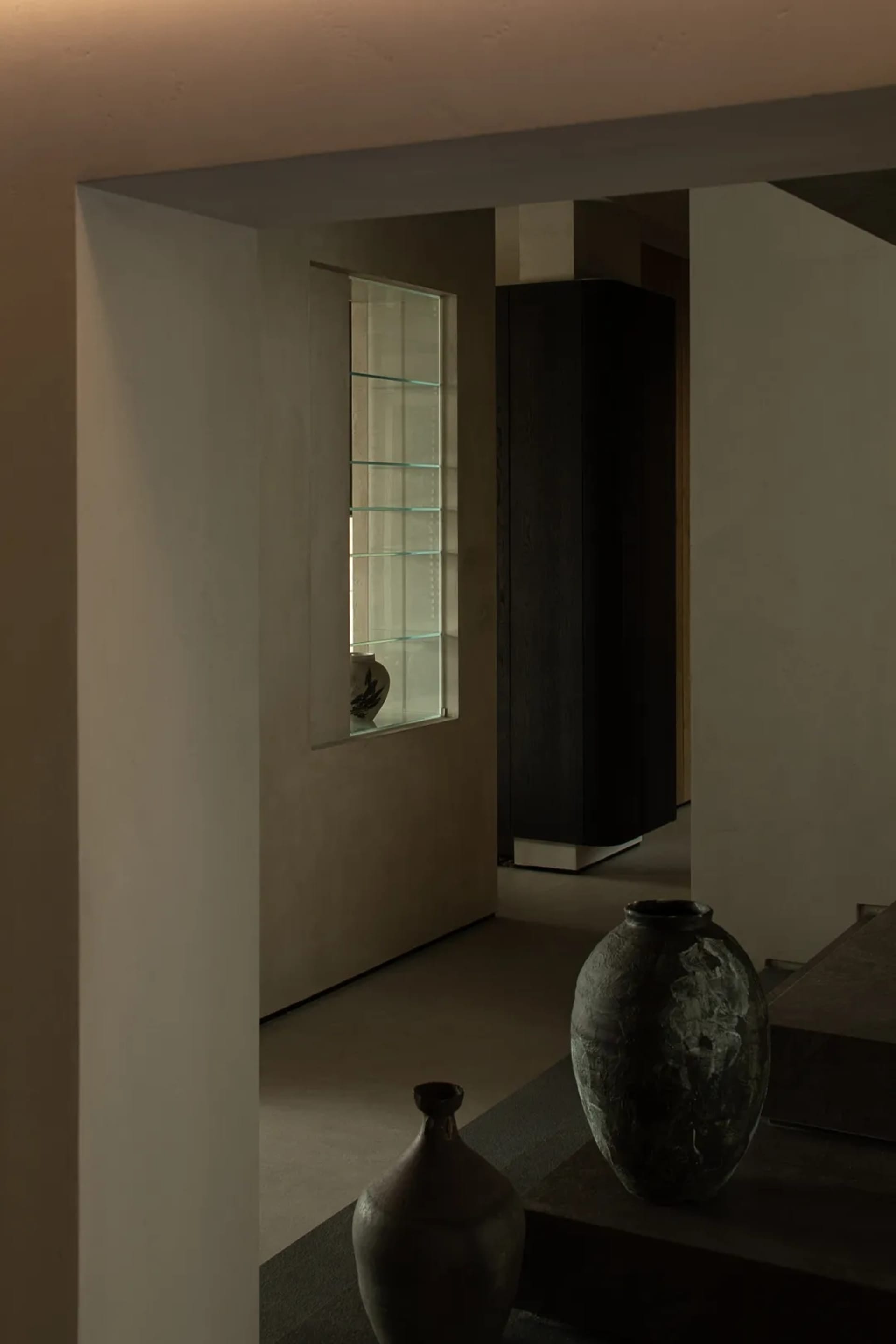 Modern living room with concrete walls and floor, featuring a large vase and a glass display case.