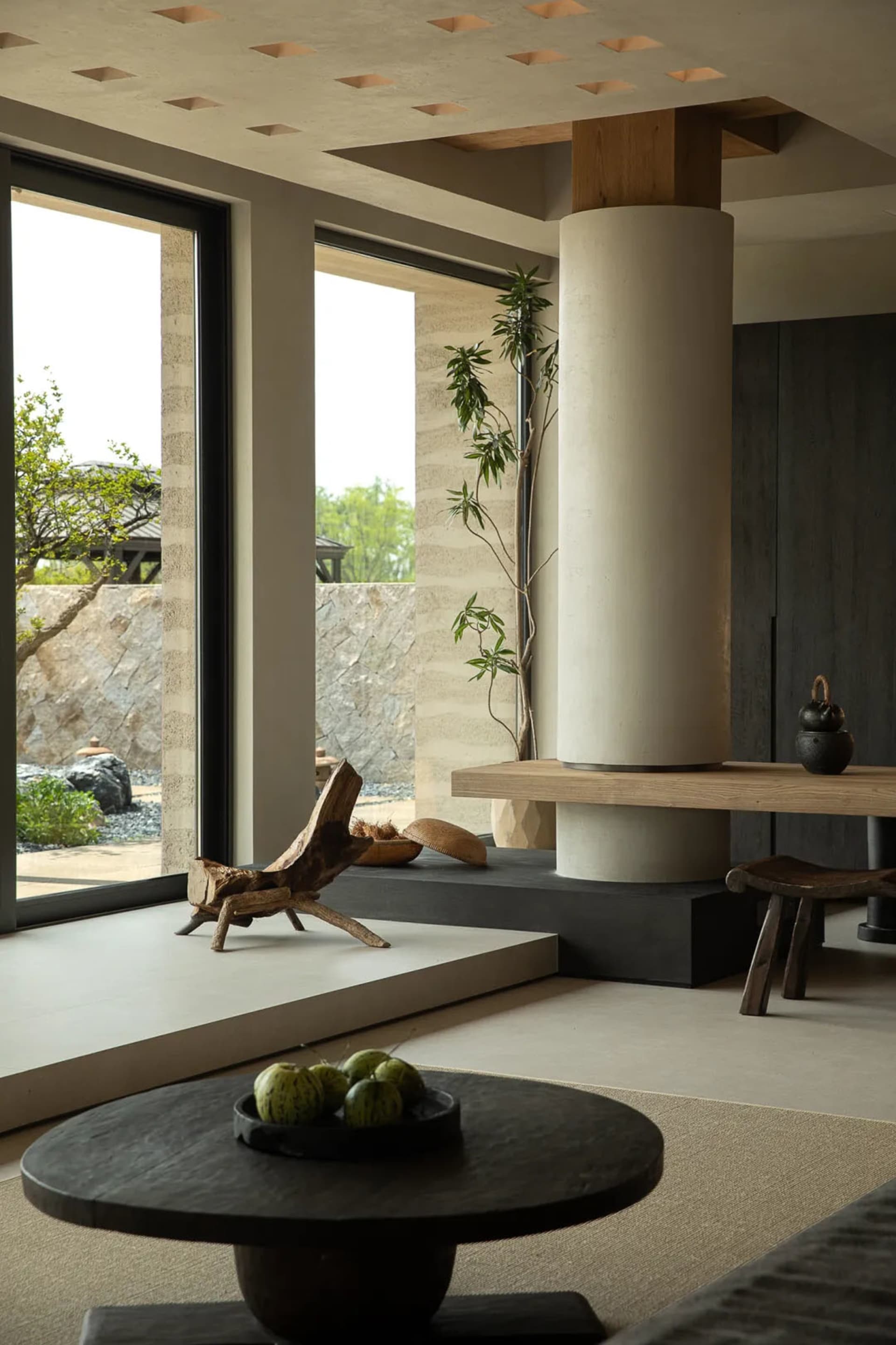Modern living room with minimalist design, featuring wooden and concrete elements, and a round wooden table with green fruit