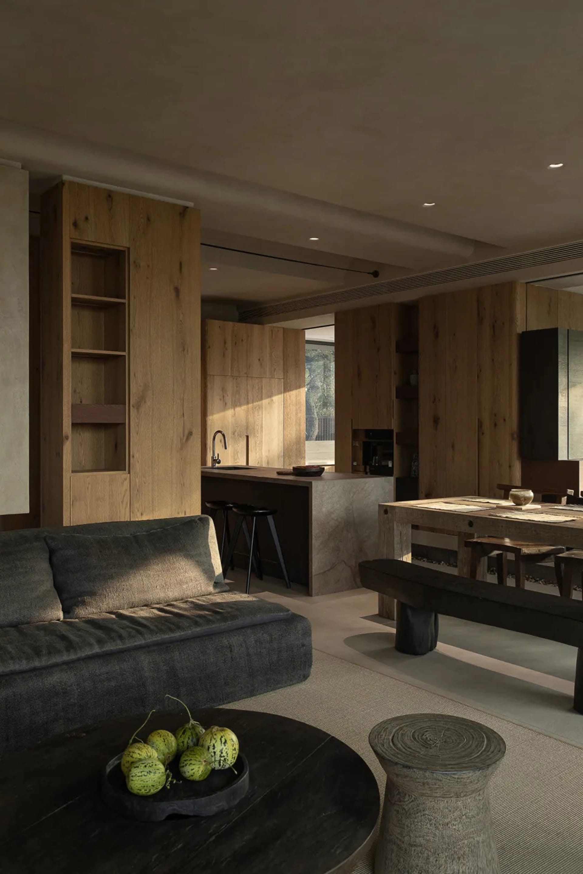 A modern living room featuring wooden furniture, including a grey sofa, a round wooden coffee table, and a wooden dining tabl
